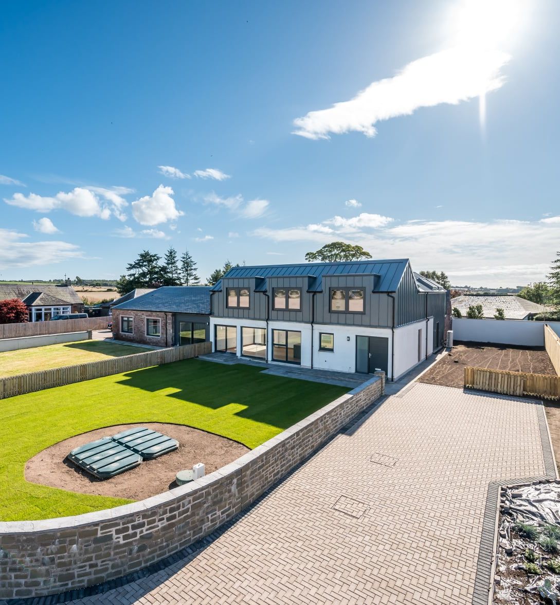 Modern two-story house with large fenced yard, green lawn, and paved driveway under a bright blue sky