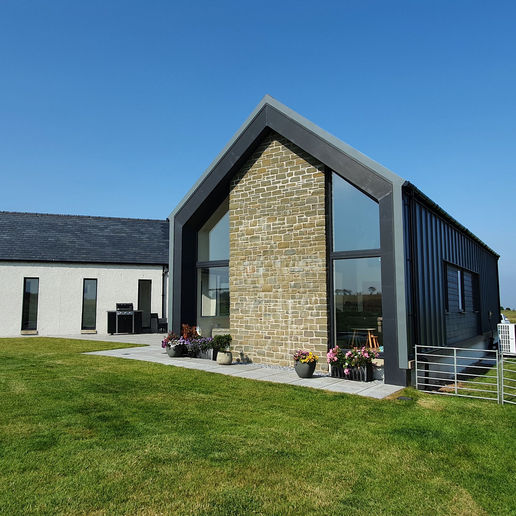 Modern house with large glass windows, a stone chimney, and a neatly mowed lawn under a clear blue sky.
