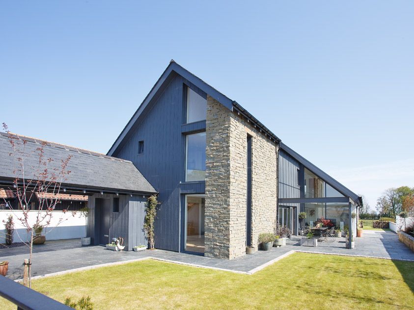Modern house with dark exterior, large windows, and stone accents in a landscaped yard.