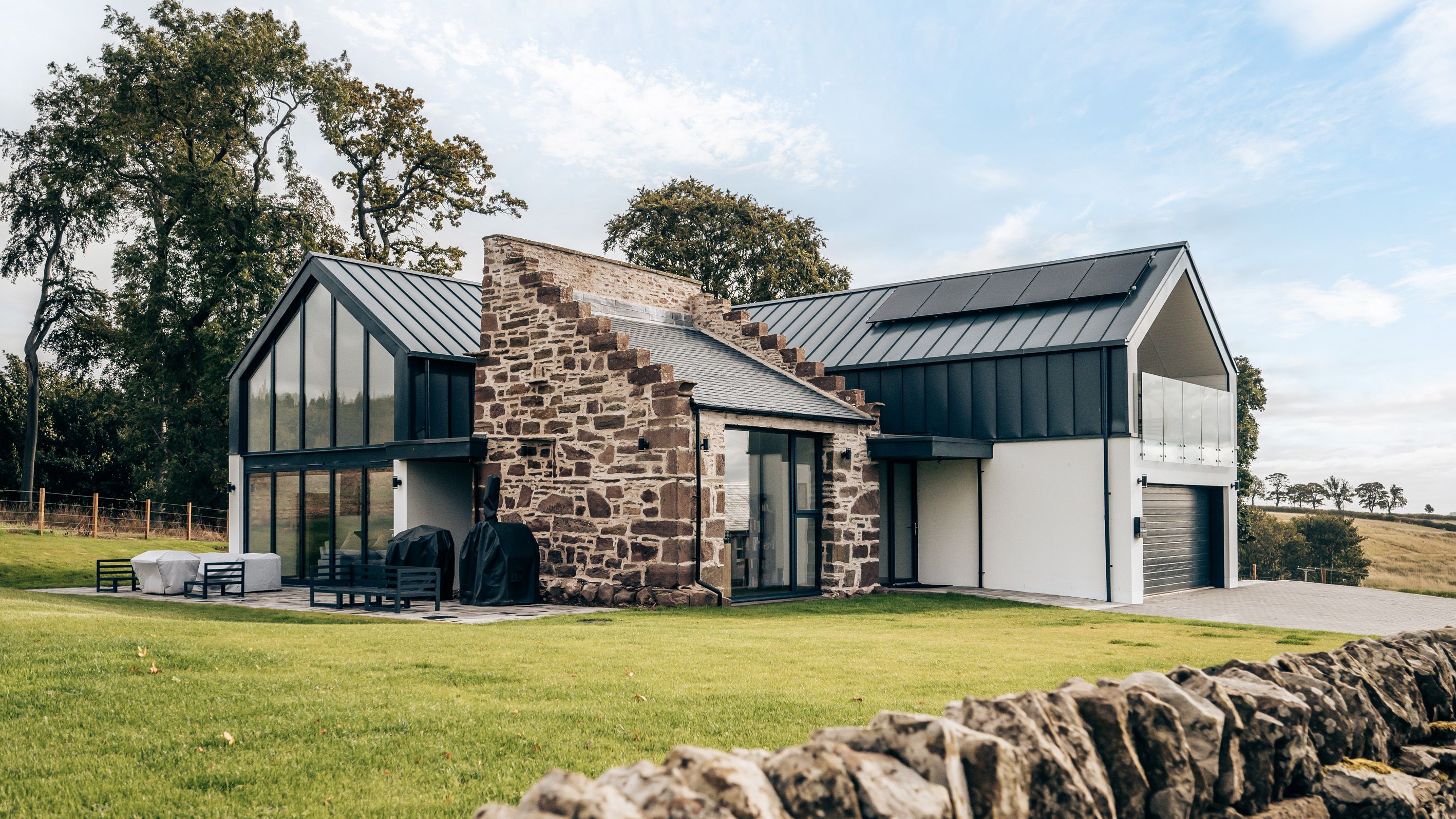Modern house with large glass windows and stone wall exterior set in the countryside.