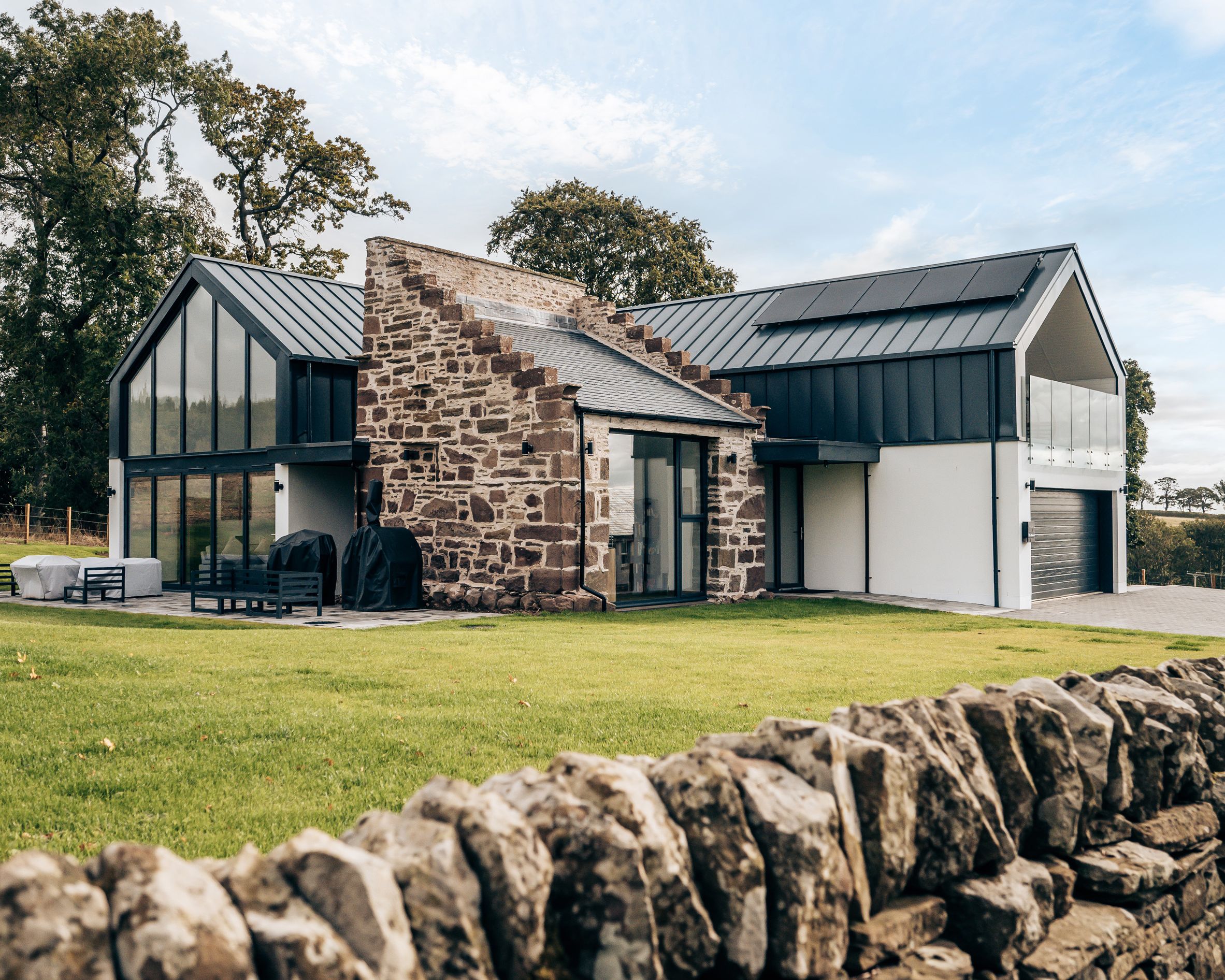 Modern house with large glass windows and stone wall exterior set in the countryside.