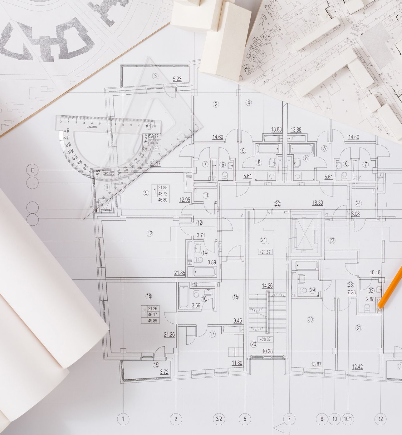 Architectural floor plan with ruler, set square, pencil, compass and white building model pieces on a desk