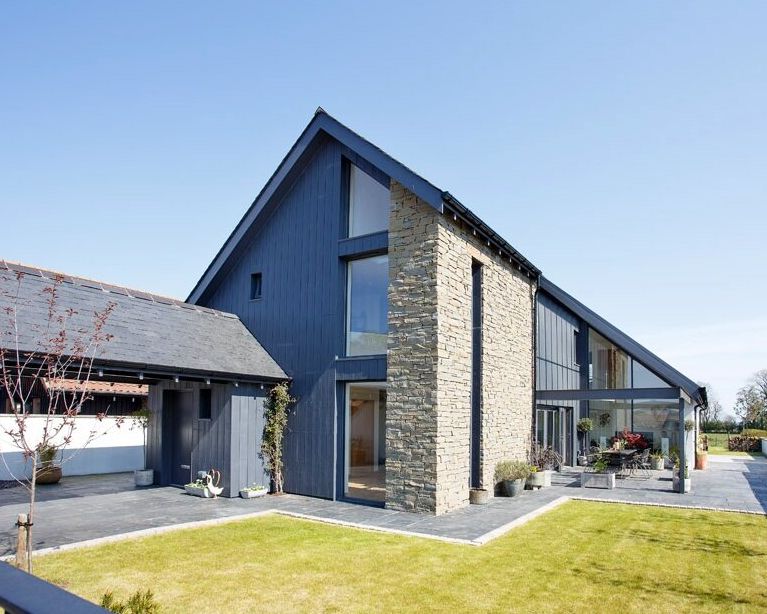 Modern house with a combination of dark wood and stone exterior, large windows, and sloped roof.