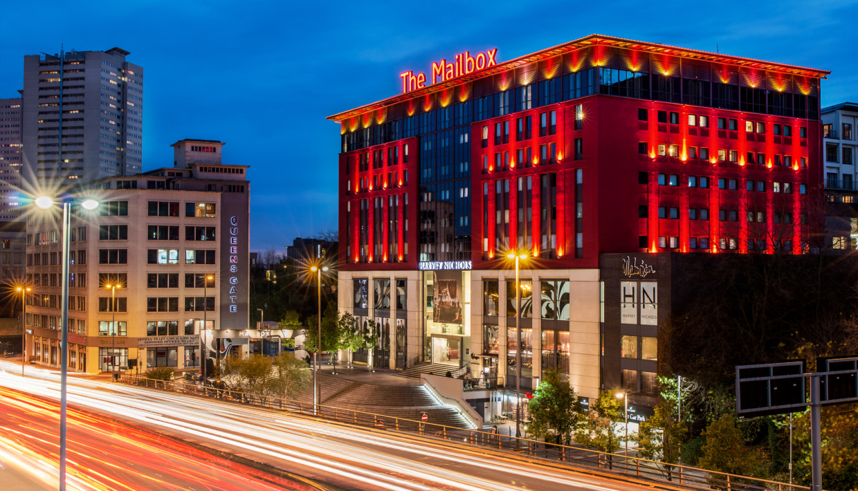 The Mailbox in Birmingham at night, with vibrant red lighting and blurred car lights.