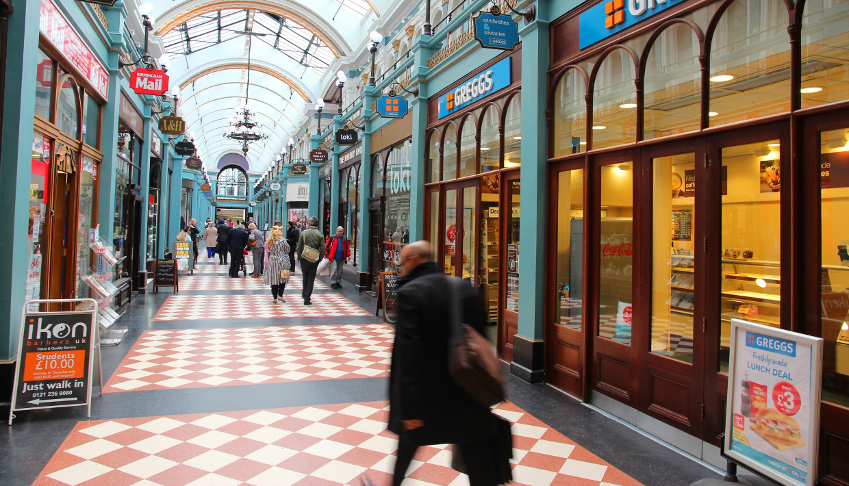 Shoppers walking through an ornate indoor arcade with Greggs and other stores on both sides.