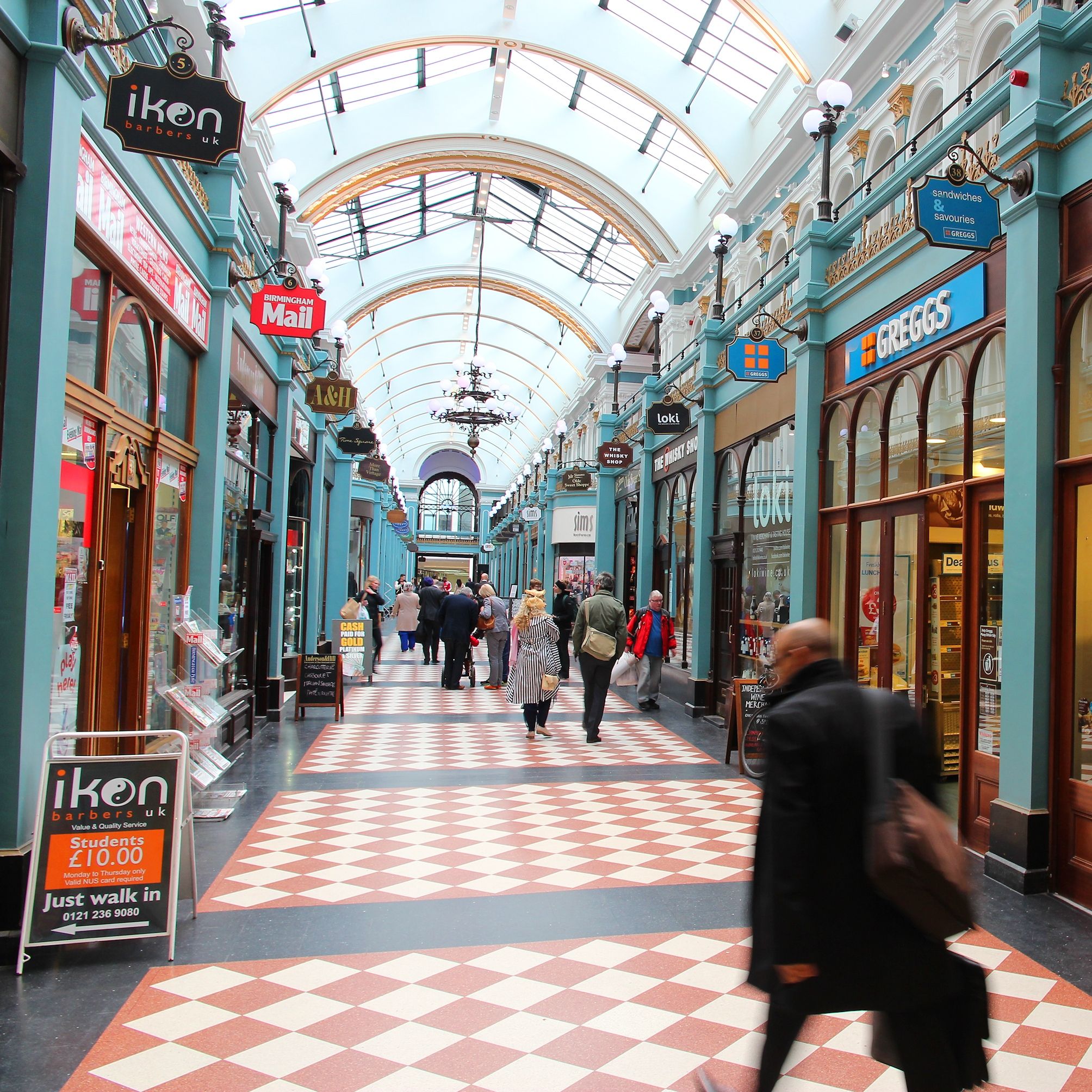Shoppers walking through an ornate indoor arcade with Greggs and other stores on both sides.