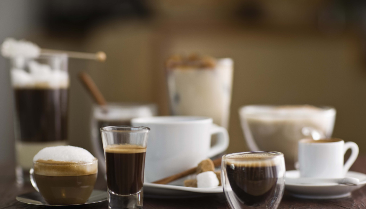 Different types of coffee drinks served in various cups and glasses on a wooden table.