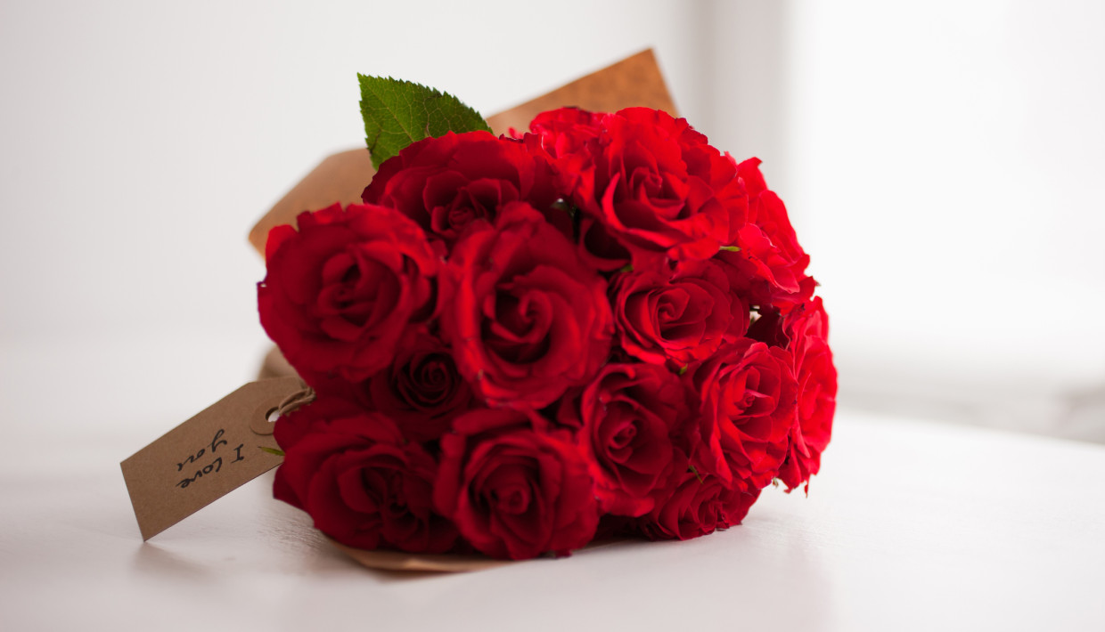 A bouquet of vibrant red roses wrapped in brown paper, with a handwritten tag reading