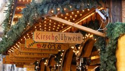 A close-up of a festive market stall decorated with string lights and pine garlands. Wooden signs display 
