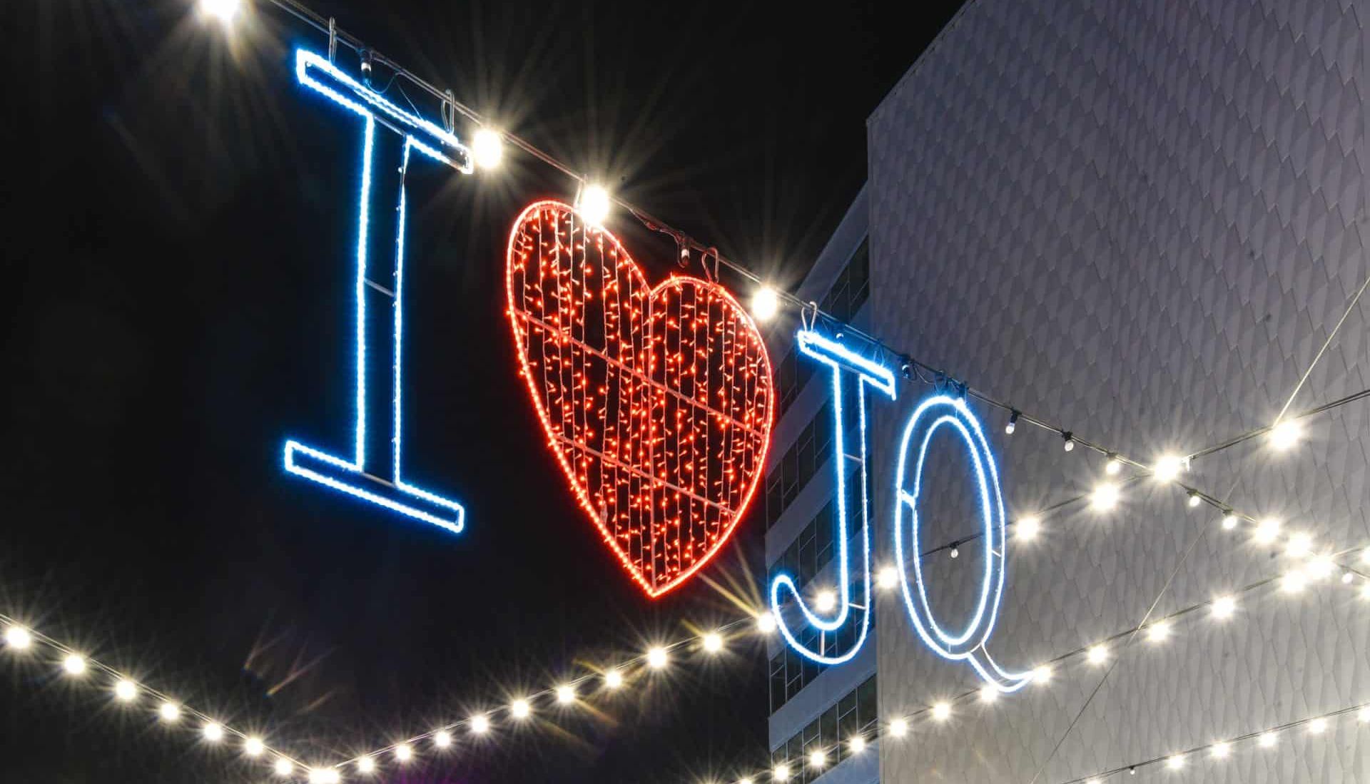 A festive crowd gathers under string lights and a glowing 