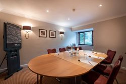 Small modern meeting room with oval table, red chairs, flip chart, and window.