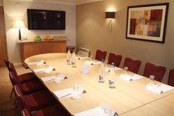 Henley Suite conference room with a long meeting table, set with water bottles, glasses, notepads, and pens, surrounded by red chairs.