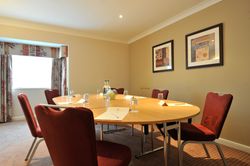 Small meeting room with a round conference table, red chairs, and framed artwork on the wall.