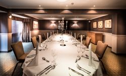 Elegant dining room set up for a formal dinner with a long table, brown chairs, white tablecloth, and a candelabra centerpiece.