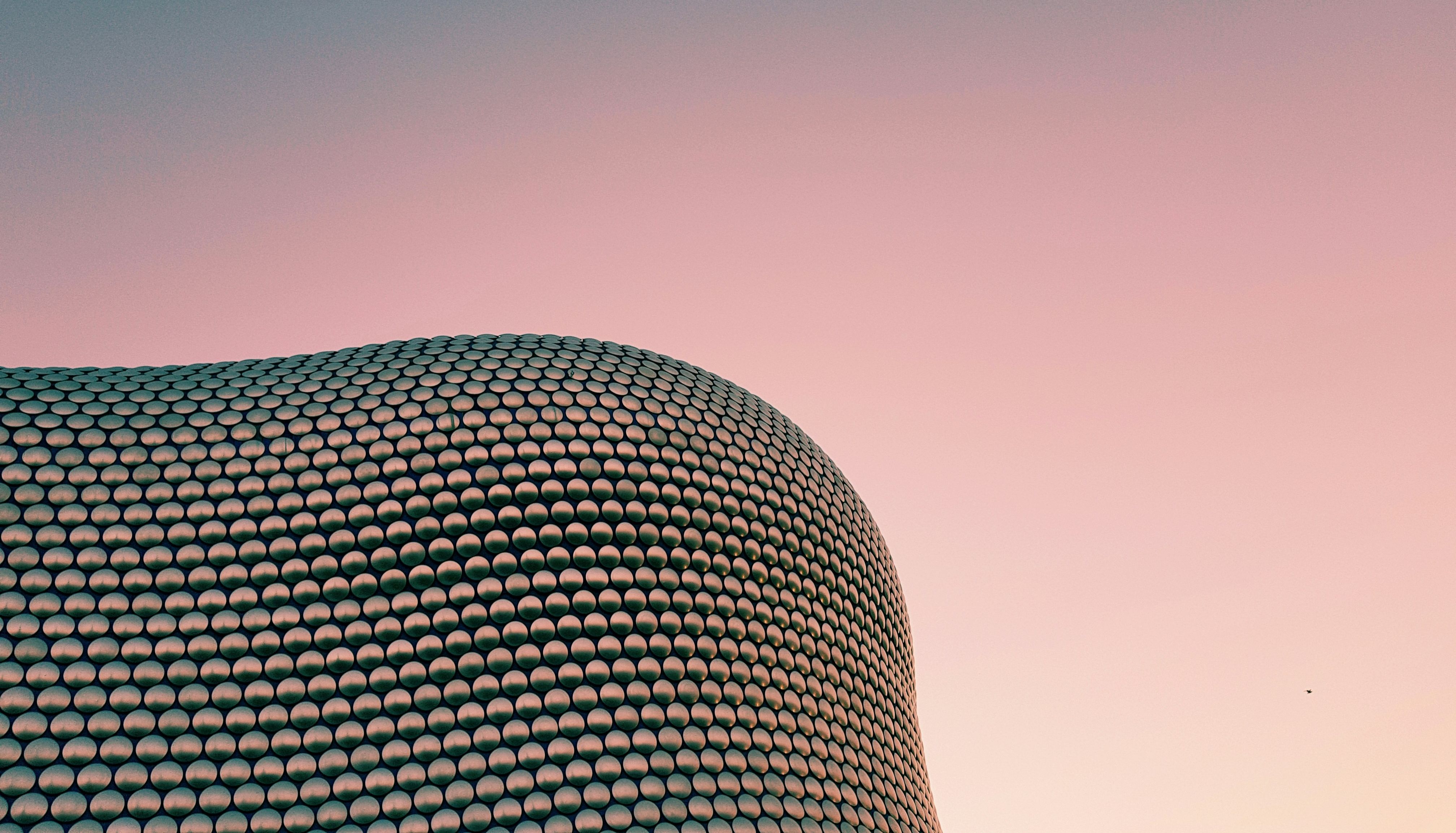 Modern building with a unique rounded facade covered in circular patterns against a pink and blue sky