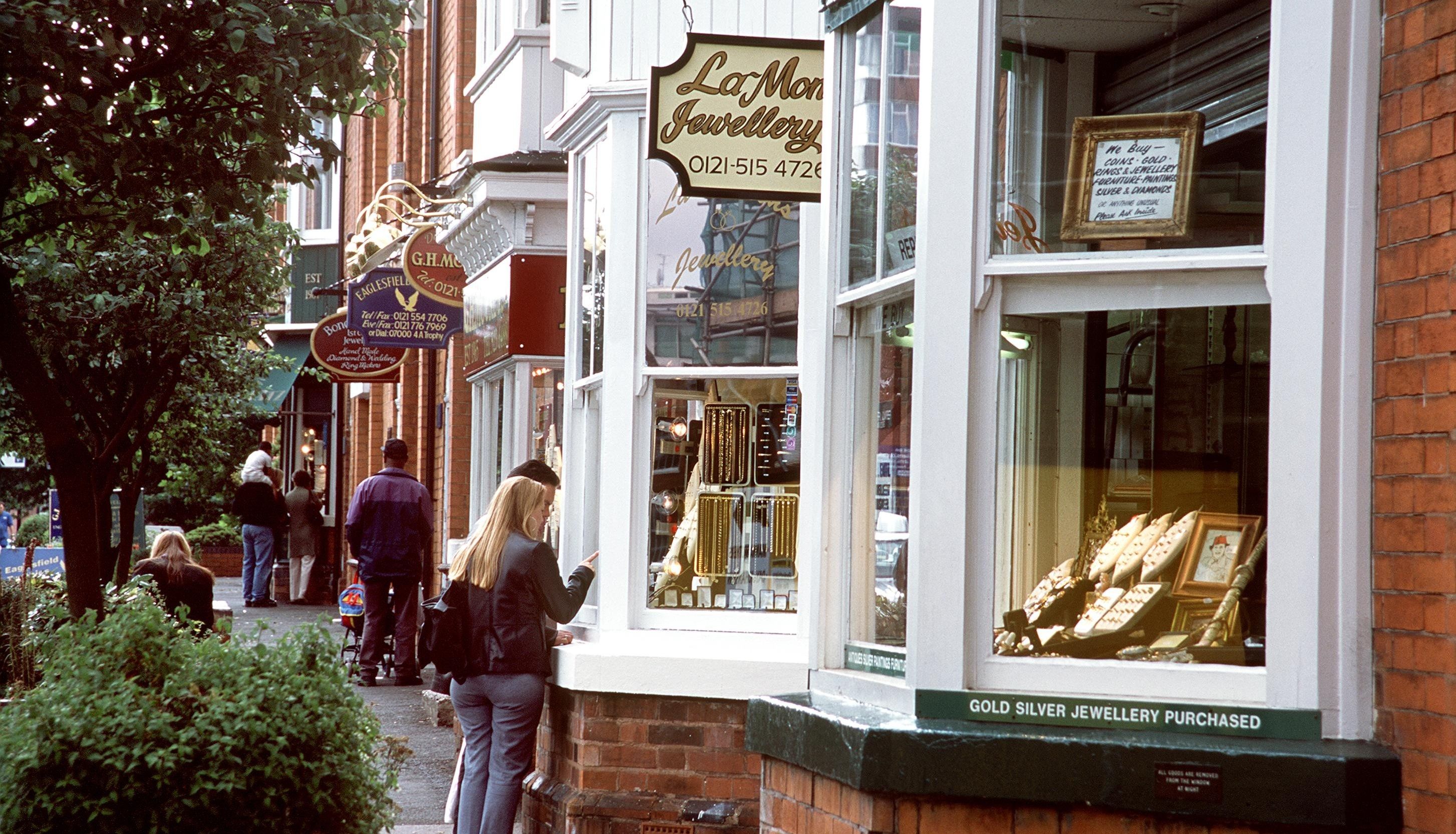 People walking on a street with various jewelry and antique shops, including LaMon Jewellery.