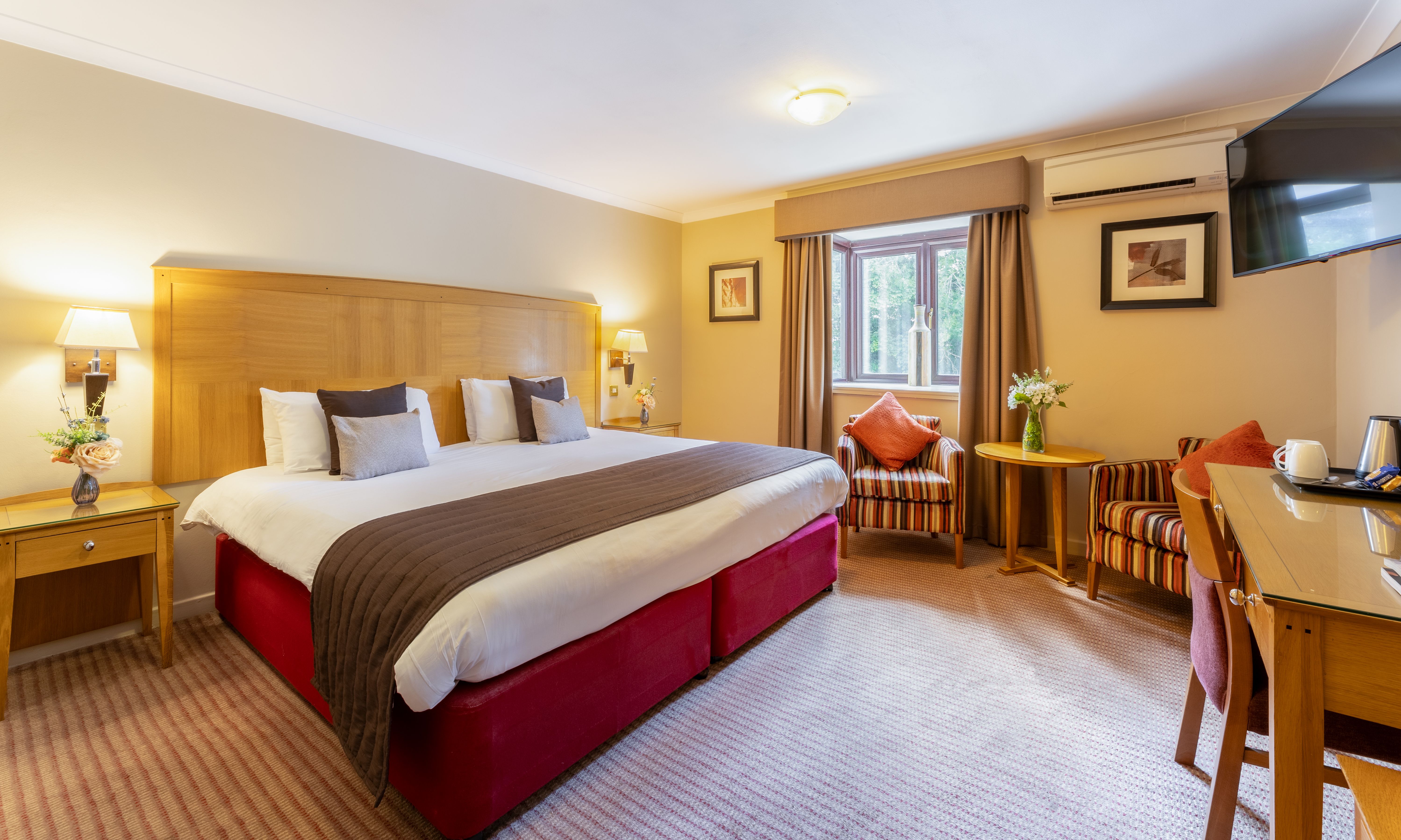 Spacious hotel room with large bed, striped armchairs, and a desk area.
