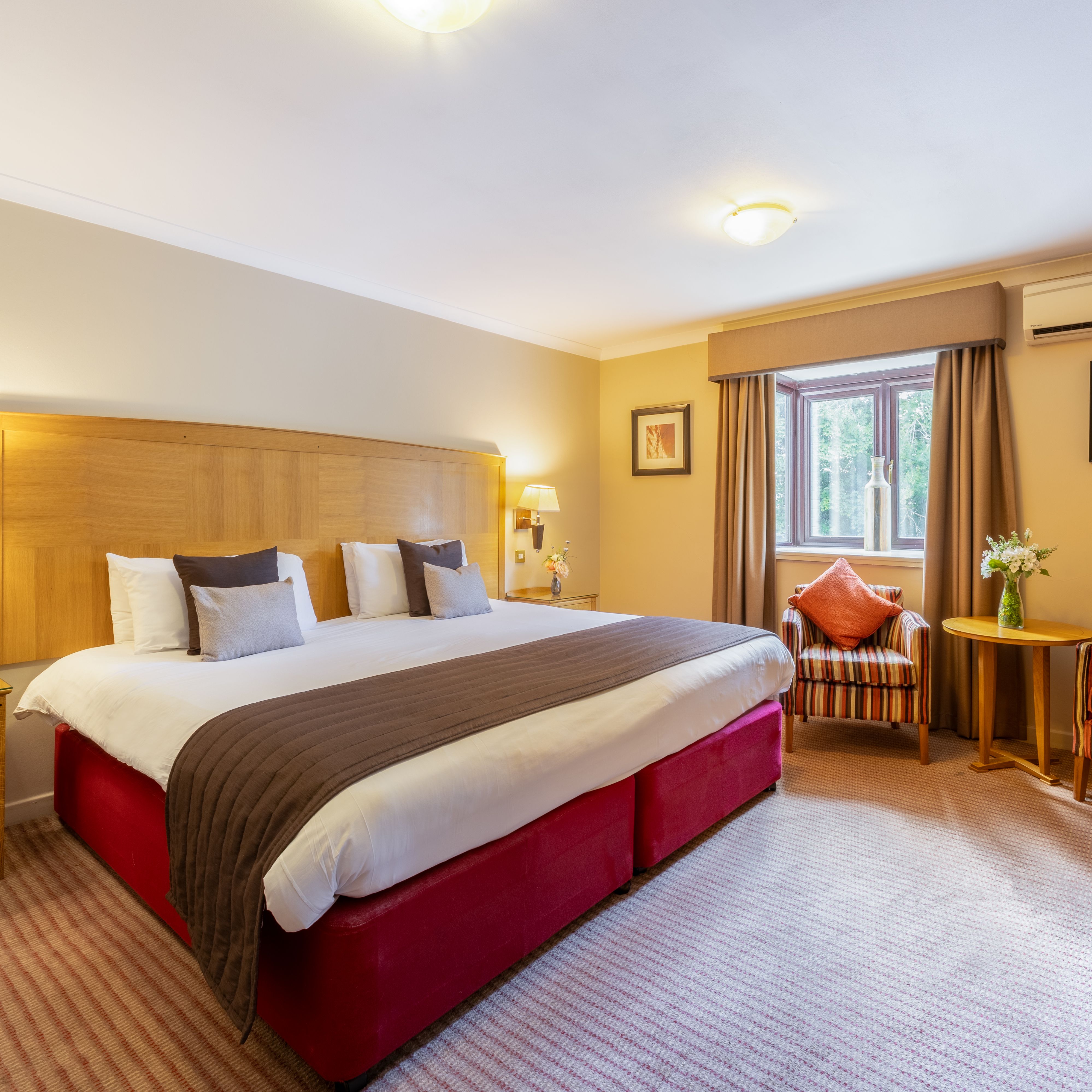 Spacious hotel room with large bed, striped armchairs, and a desk area.