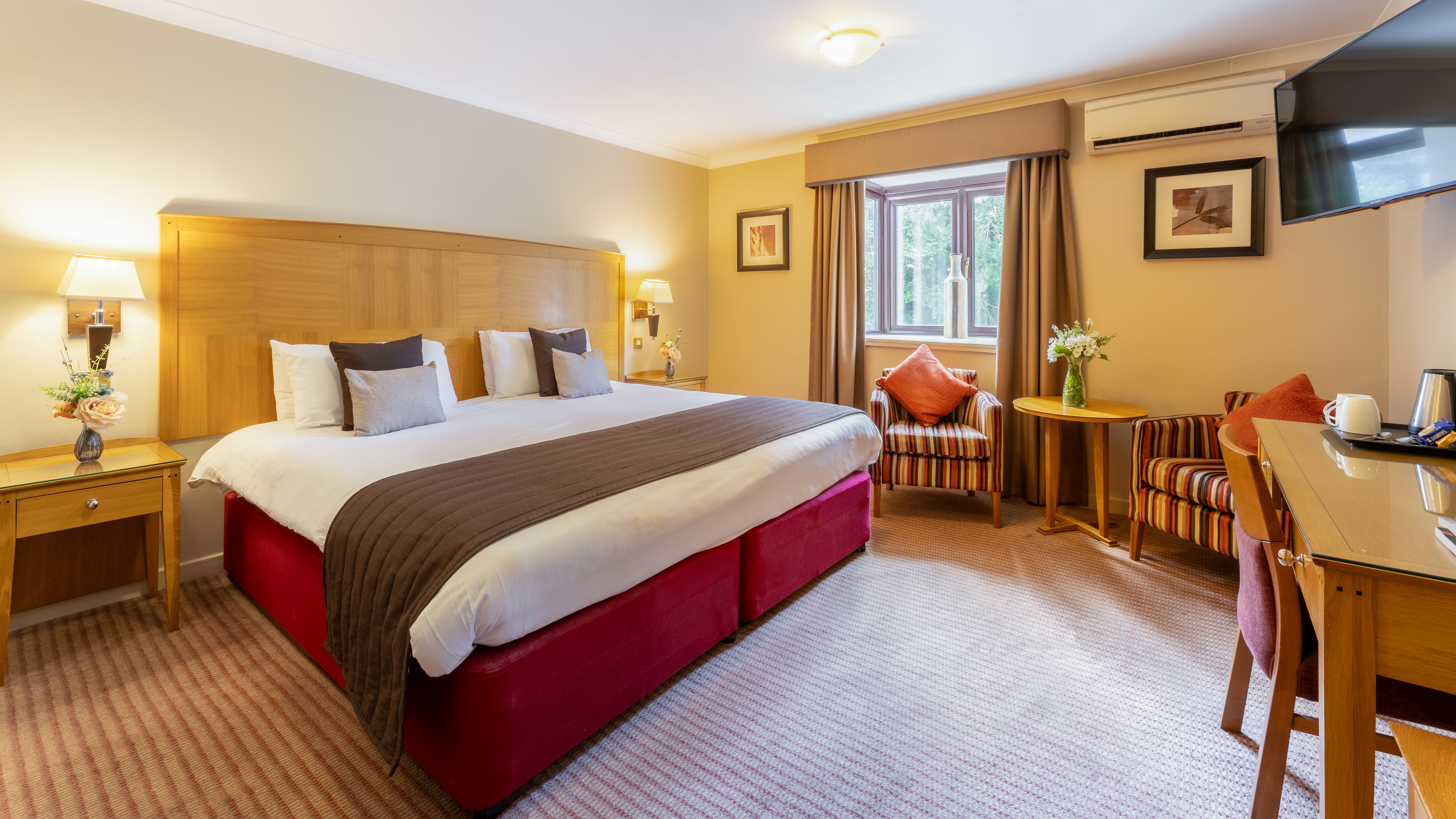 Spacious hotel room with large bed, striped armchairs, and a desk area.