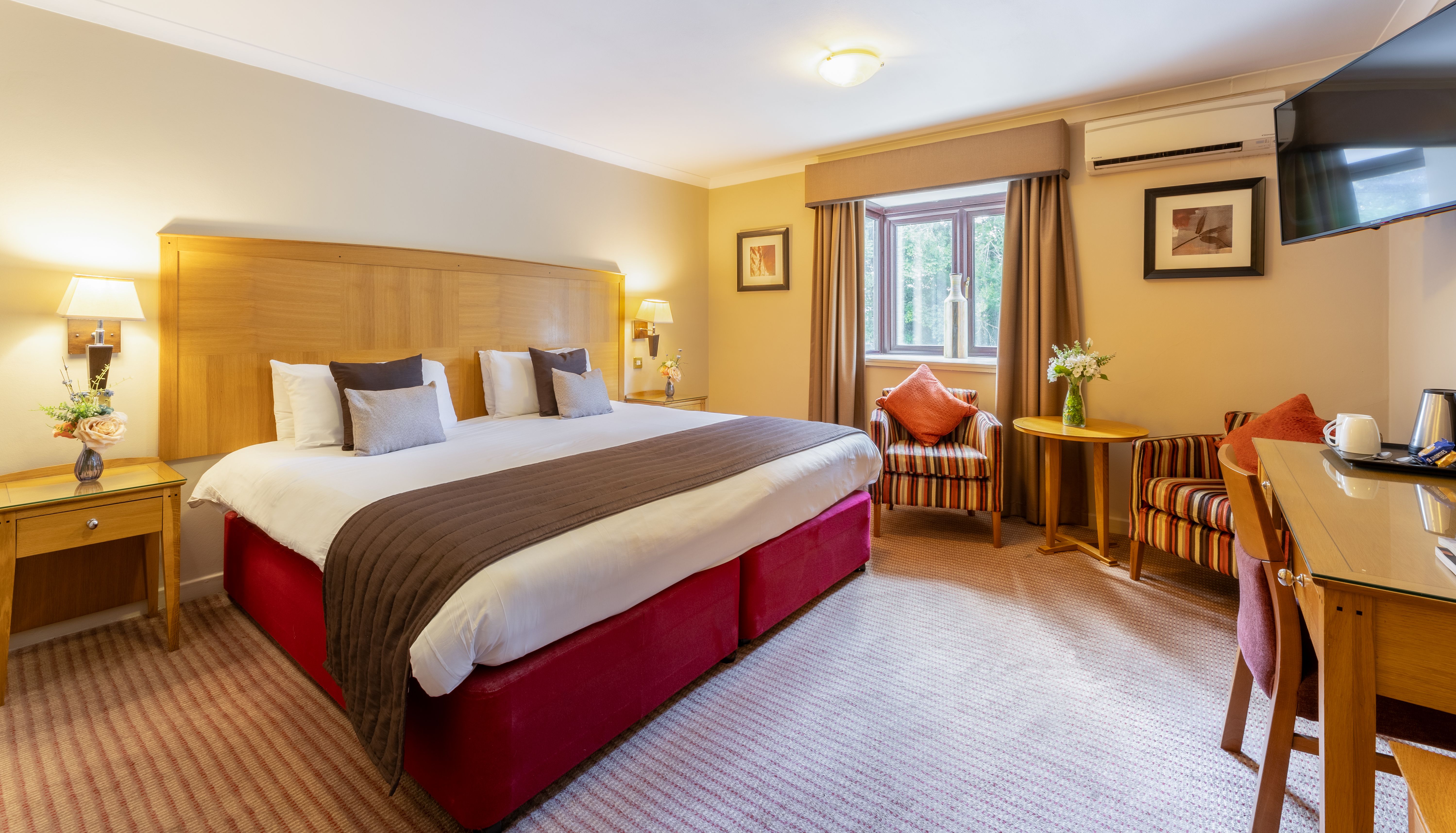 Spacious hotel room with large bed, striped armchairs, and a desk area.