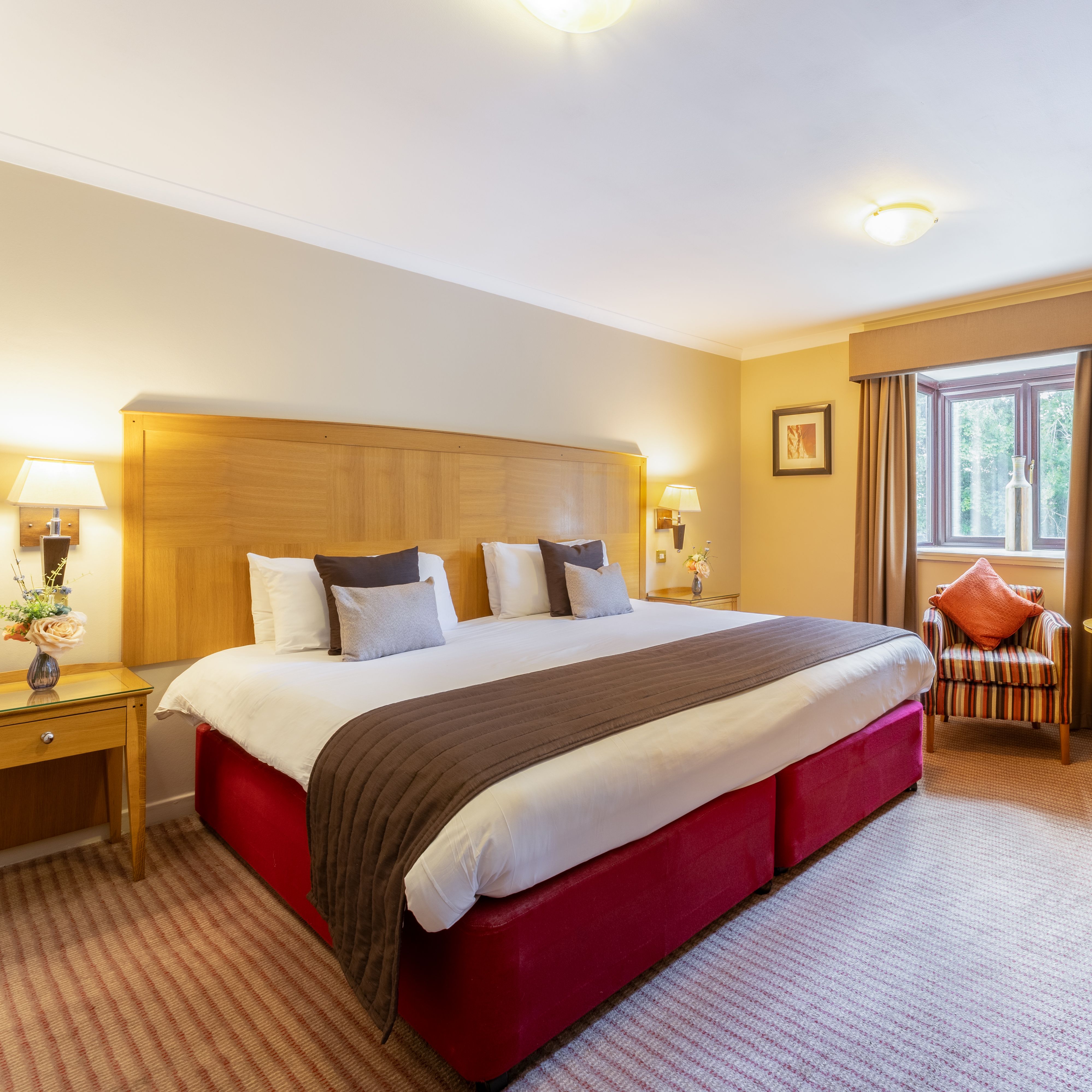 Spacious hotel room with large bed, striped armchairs, and a desk area.