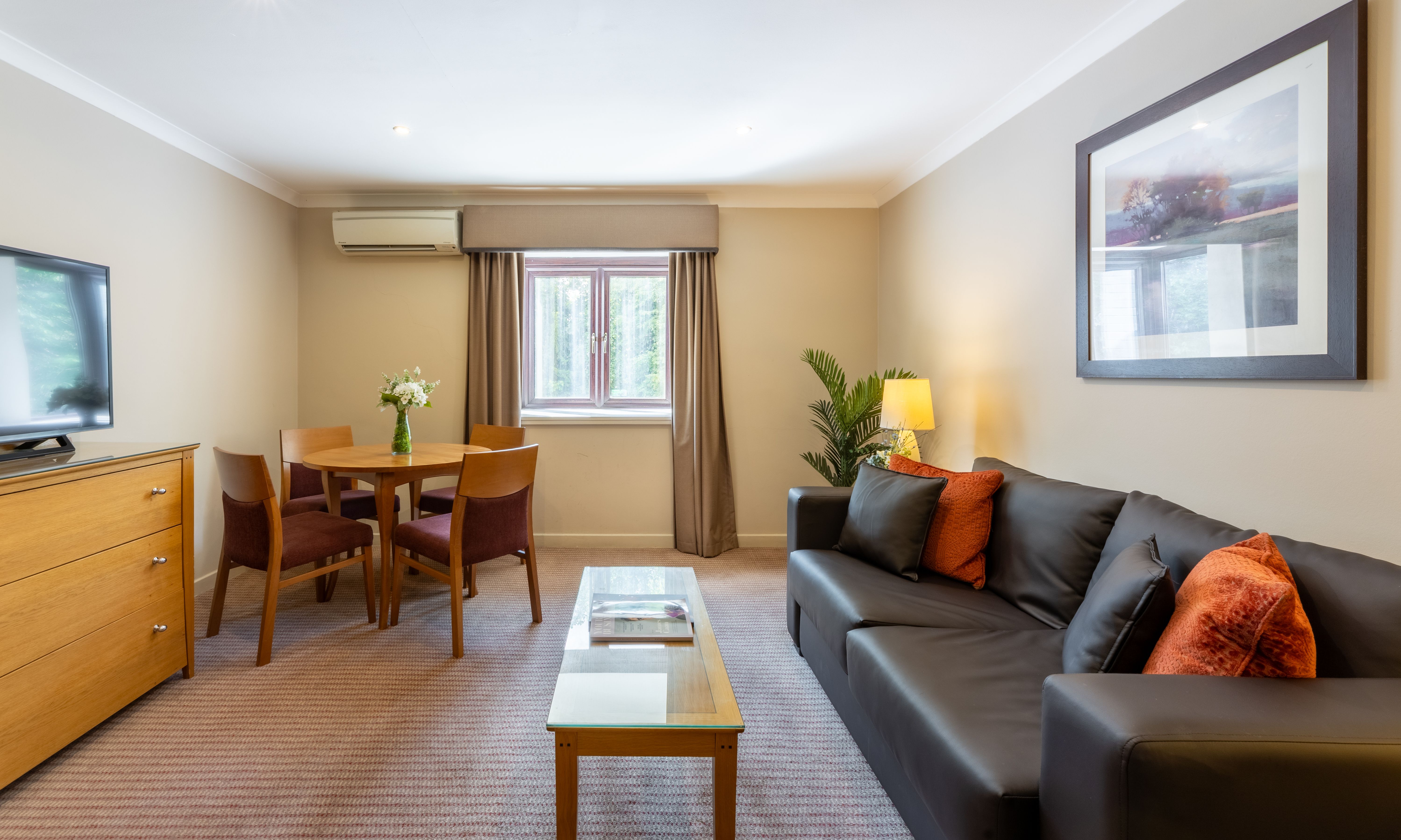 Modern lounge area with a black leather sofa, coffee table, dining set, and television.