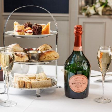 Afternoon tea setup with assorted sandwiches, scones, cakes, a bottle of prosecco, and two glasses of sparkling wine.