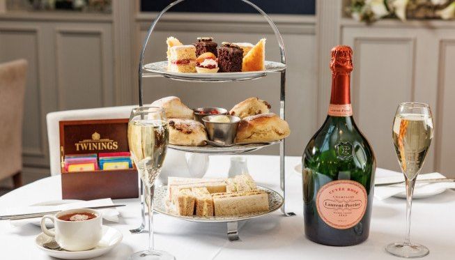 Afternoon tea setup with assorted sandwiches, scones, cakes, a bottle of prosecco, and two glasses of sparkling wine.