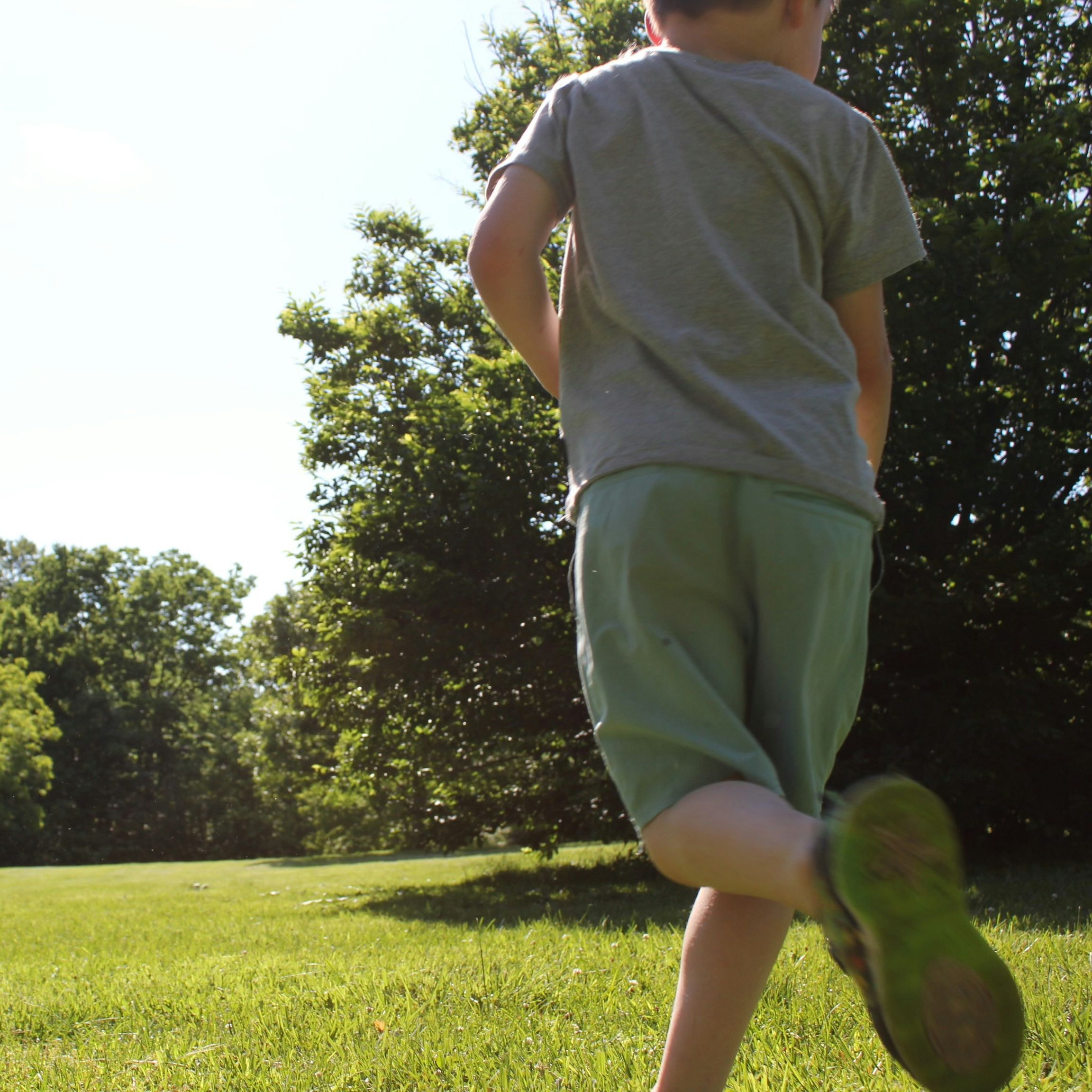 Child running across a sunny grassy field beside trees