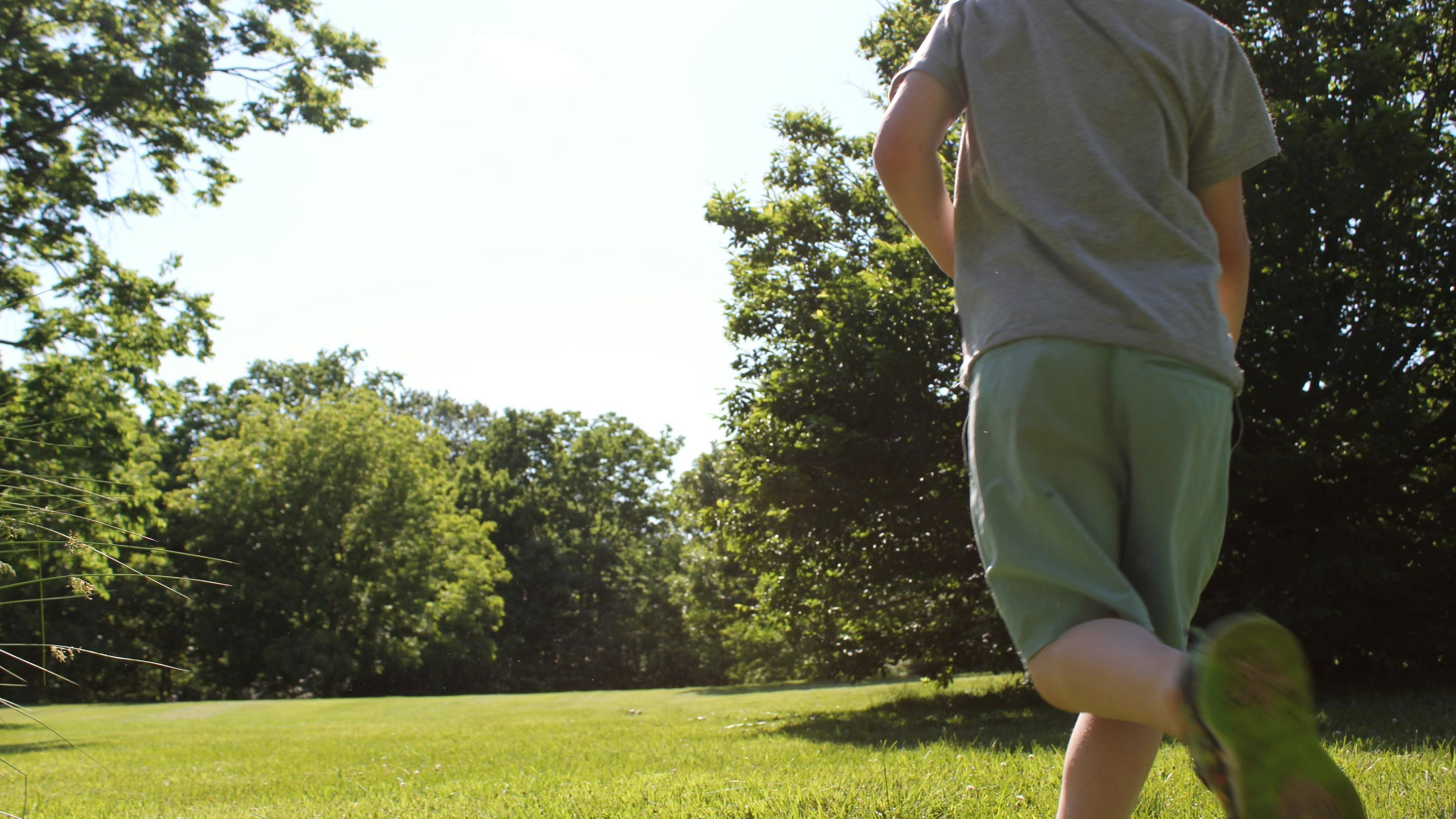 Child running across a sunny grassy field beside trees
