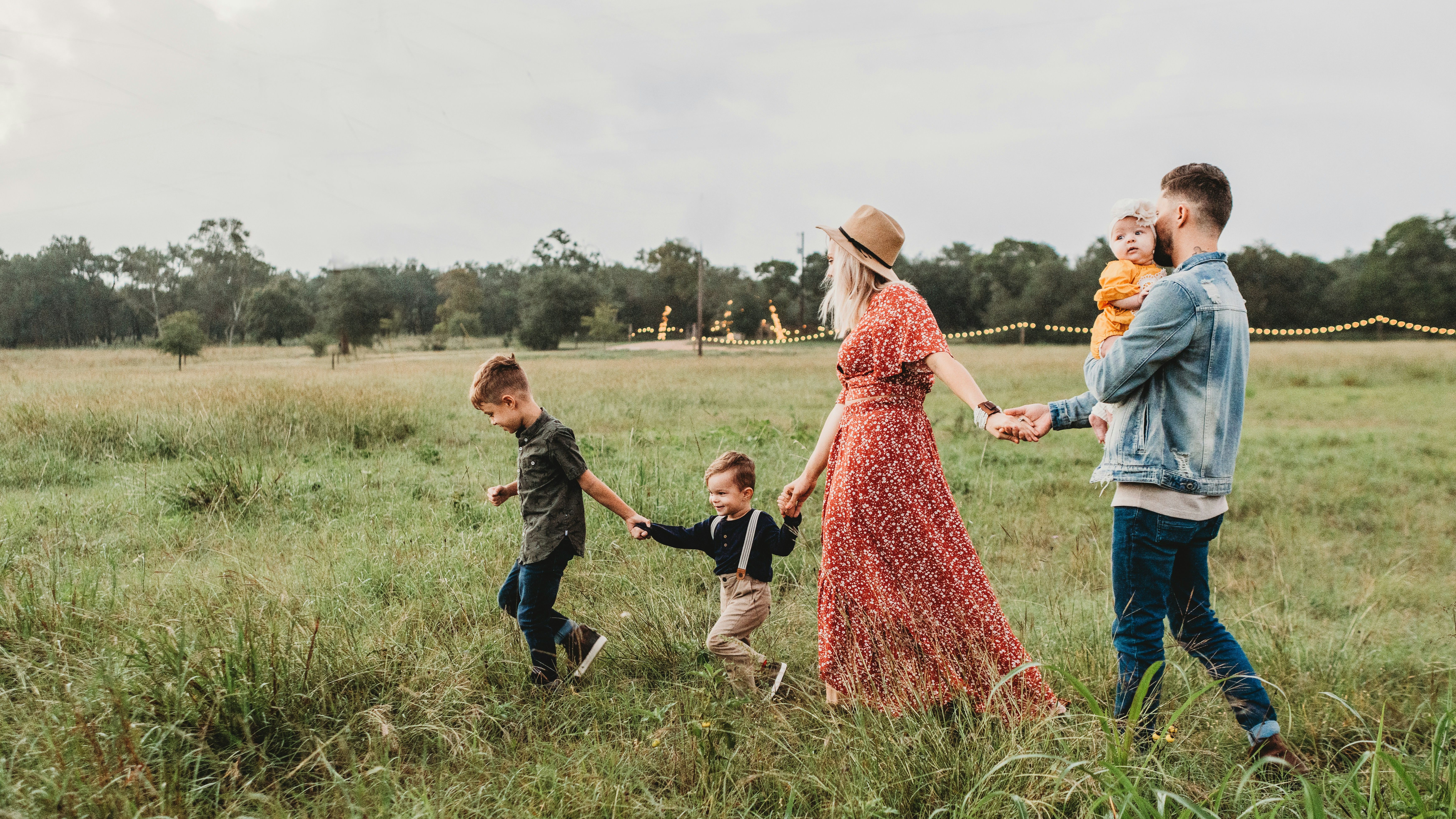 Family walking hand in hand through a grassy field at dusk