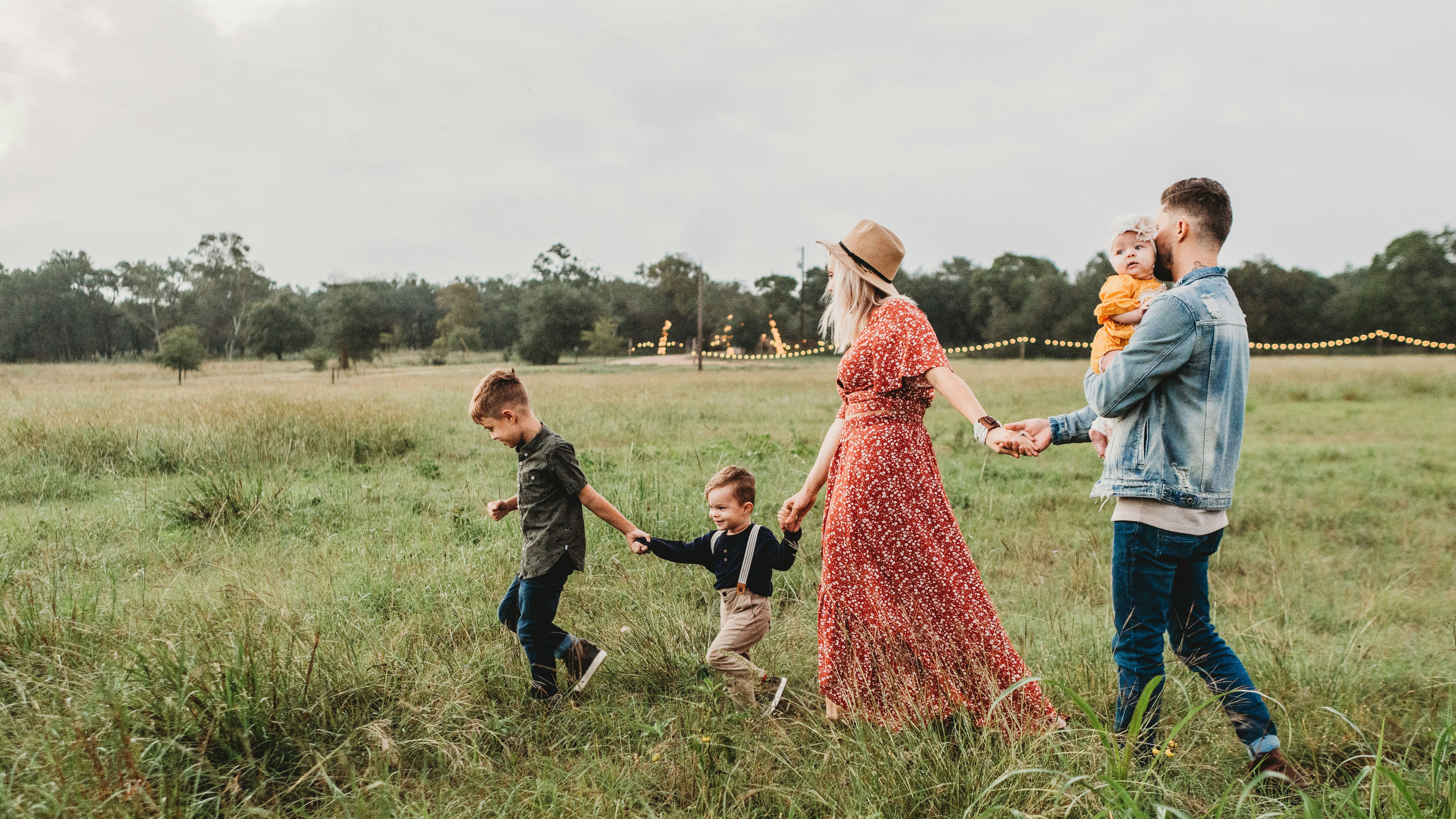 Family walking hand in hand through a grassy field at dusk