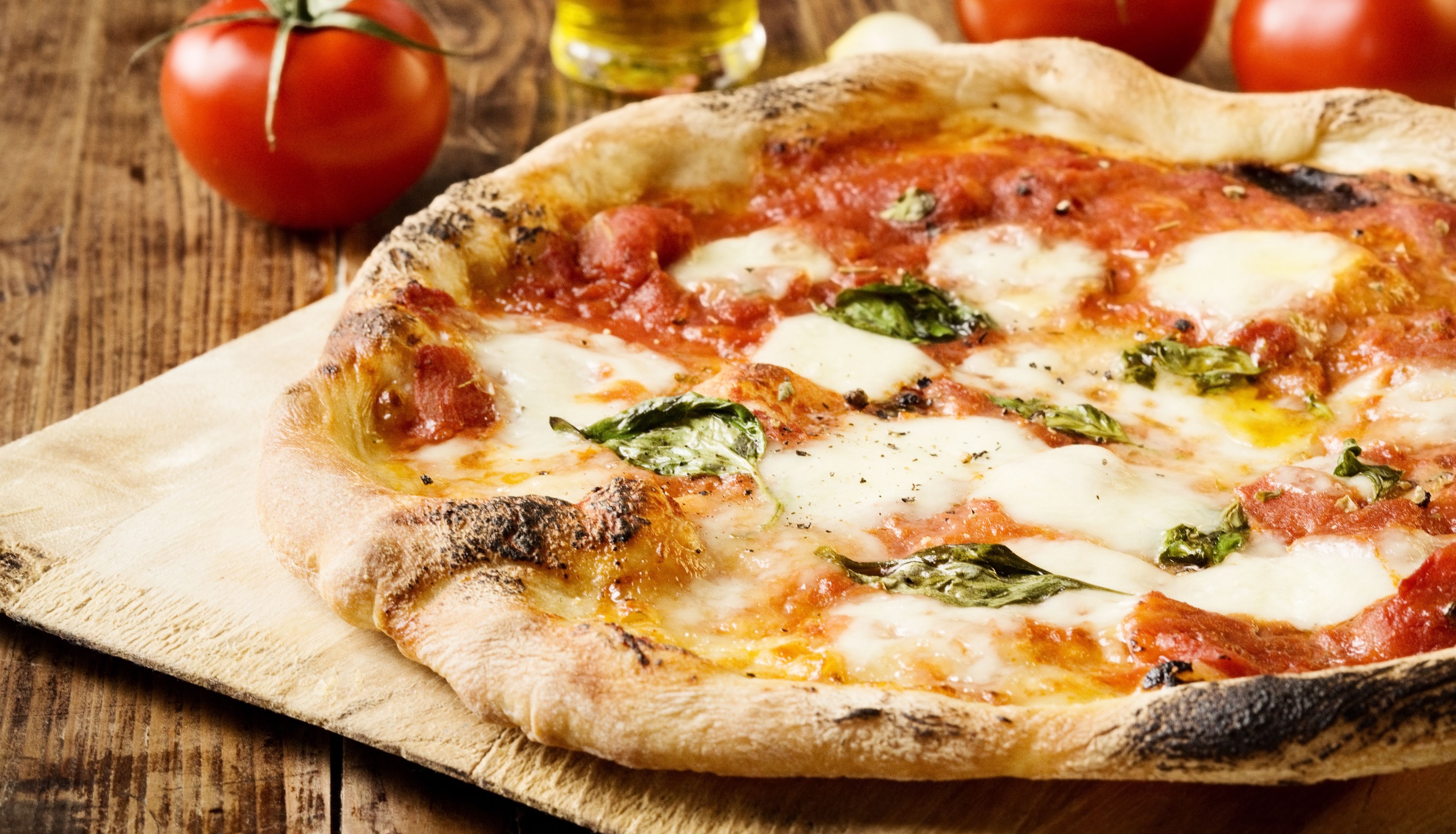 Margherita pizza with melted mozzarella, tomato sauce and basil on a wooden board, with fresh tomatoes and olive oil in the background