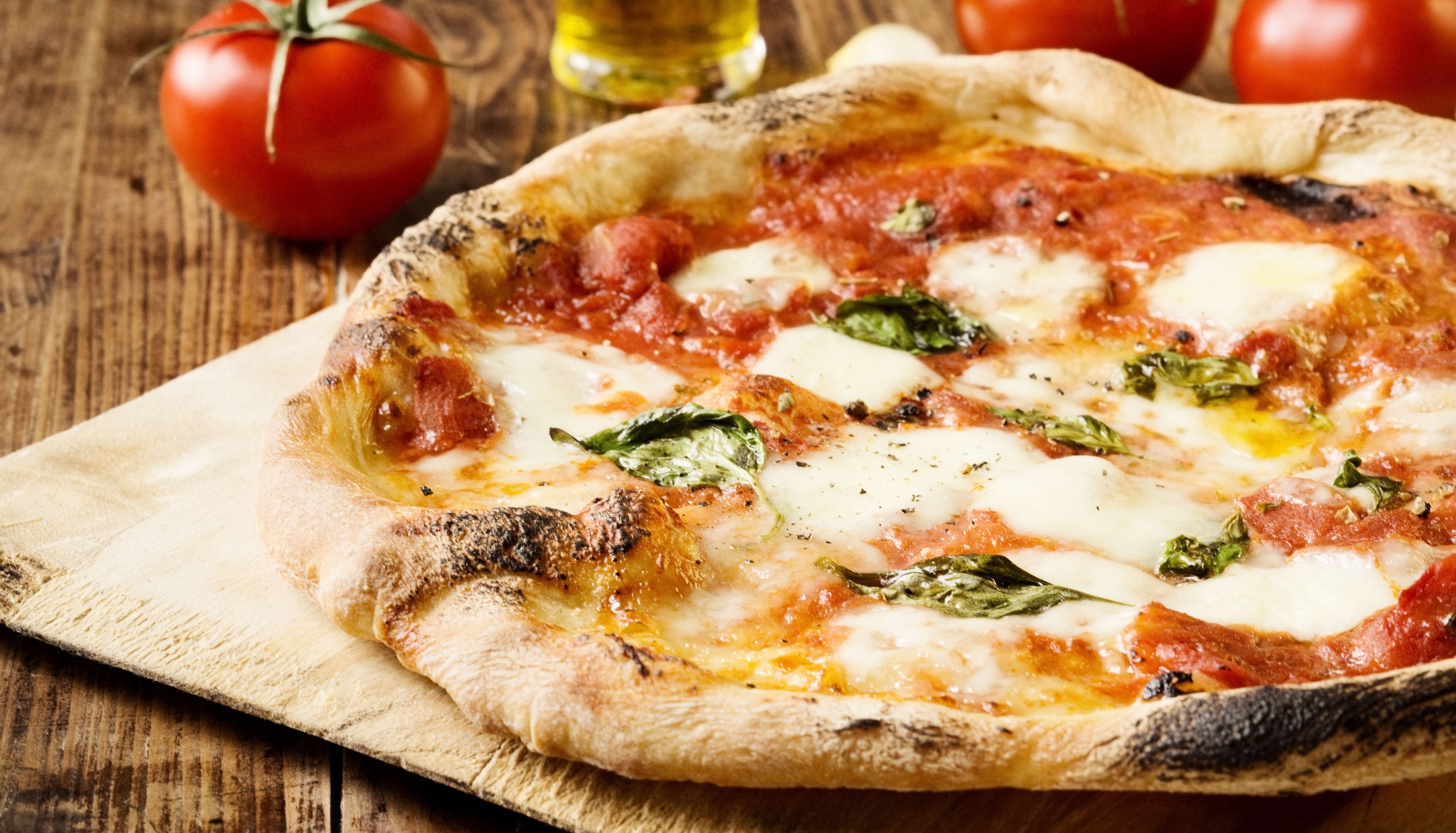 Margherita pizza with melted mozzarella, tomato sauce and basil on a wooden board, with fresh tomatoes and olive oil in the background
