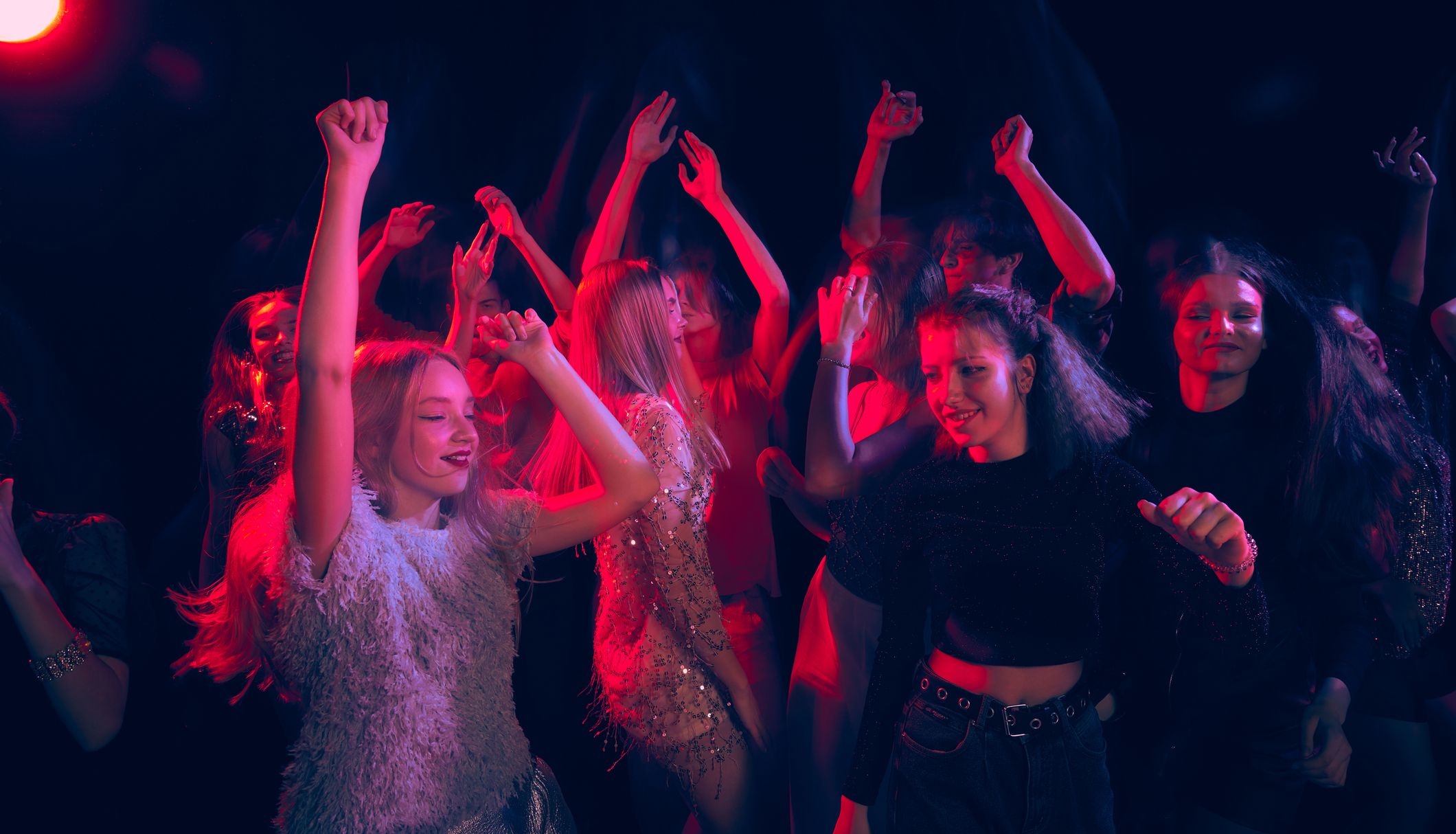 Young people dancing with hands raised under red and blue club lights