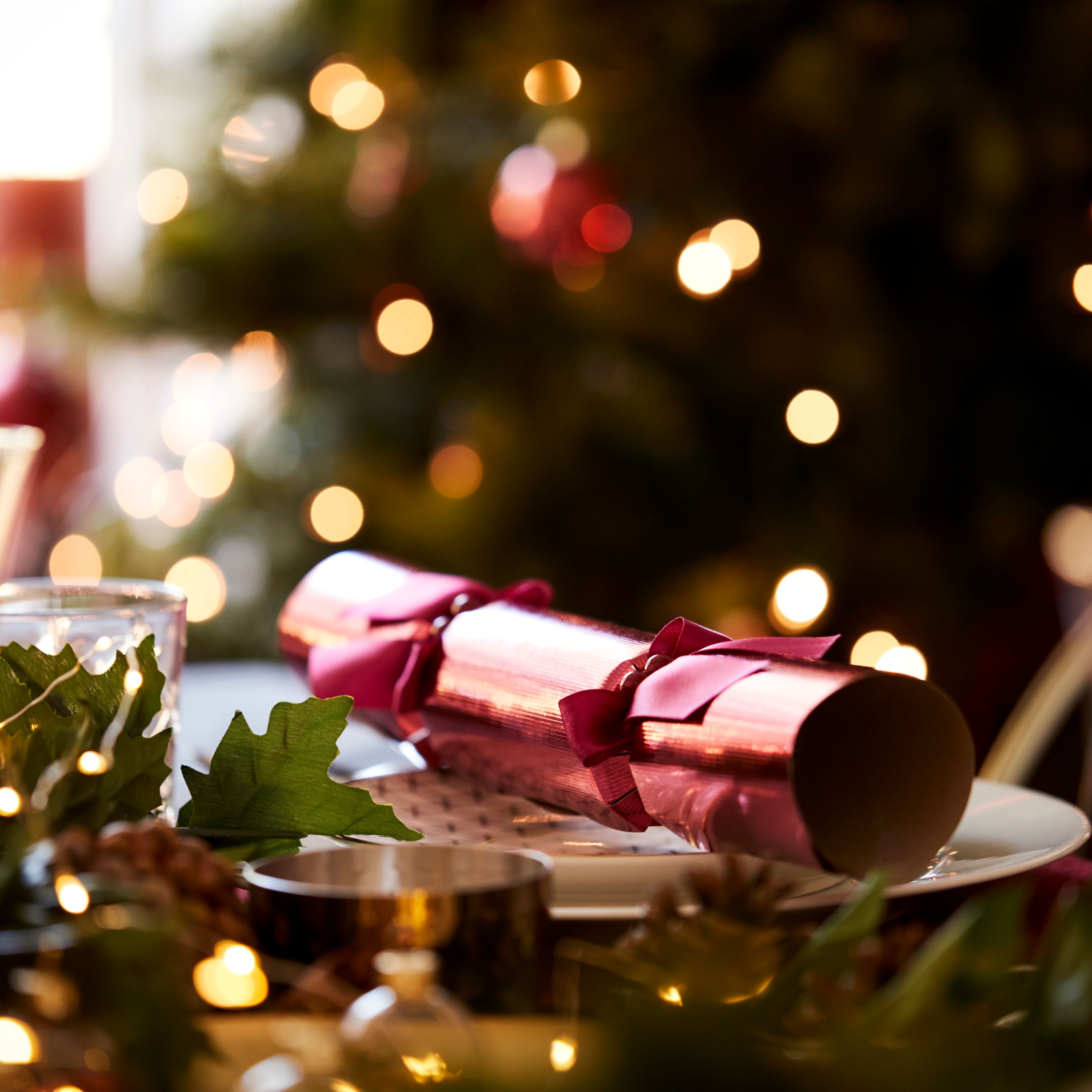 Christmas table setting with pink cracker, festive greenery and blurred fairy lights in the background