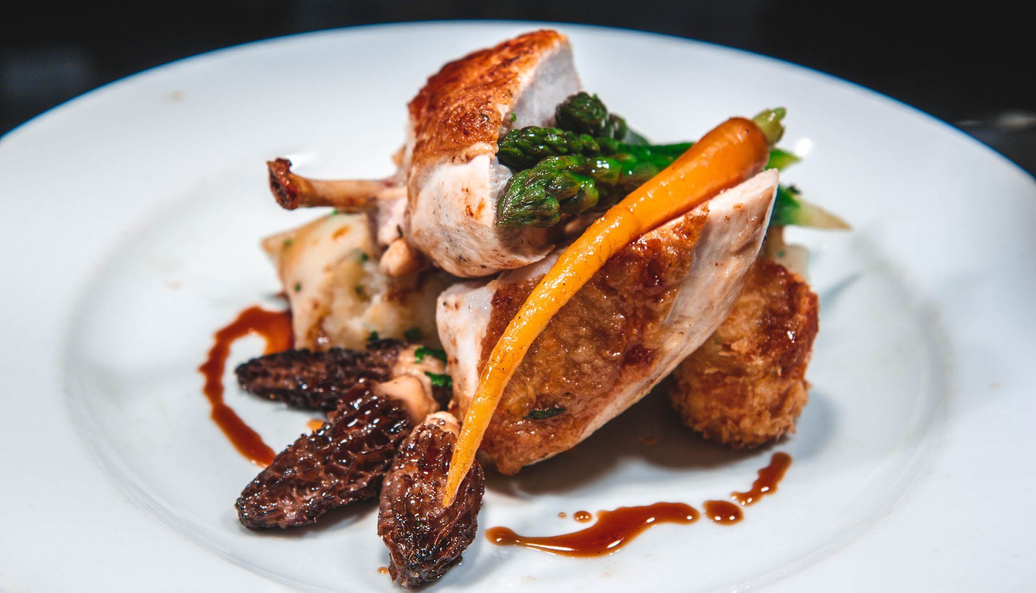 Gourmet roasted poultry with asparagus, carrot, morel mushrooms and sauce on a white plate