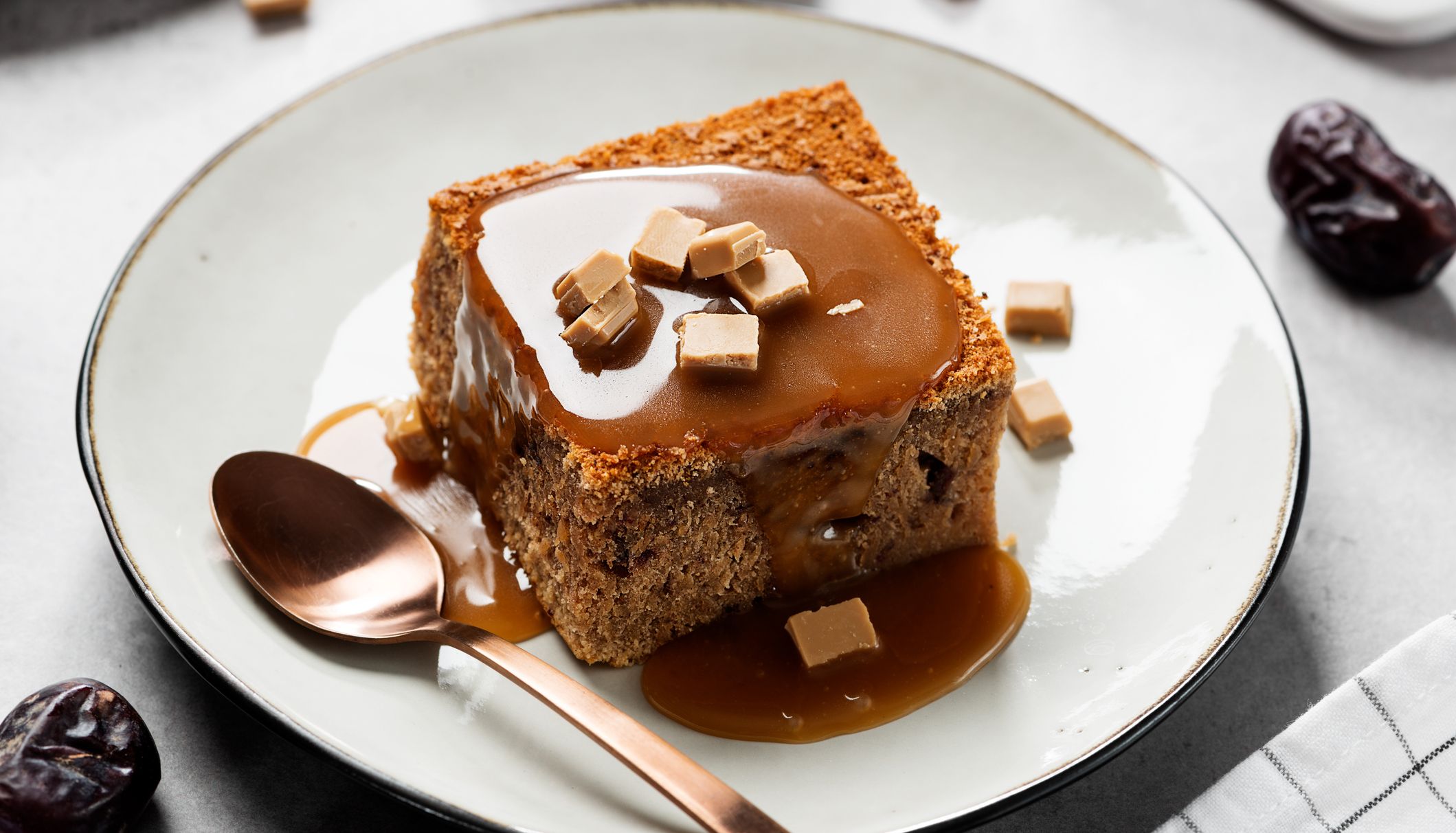 Sticky toffee pudding with toffee sauce and fudge pieces on a white plate with a spoon