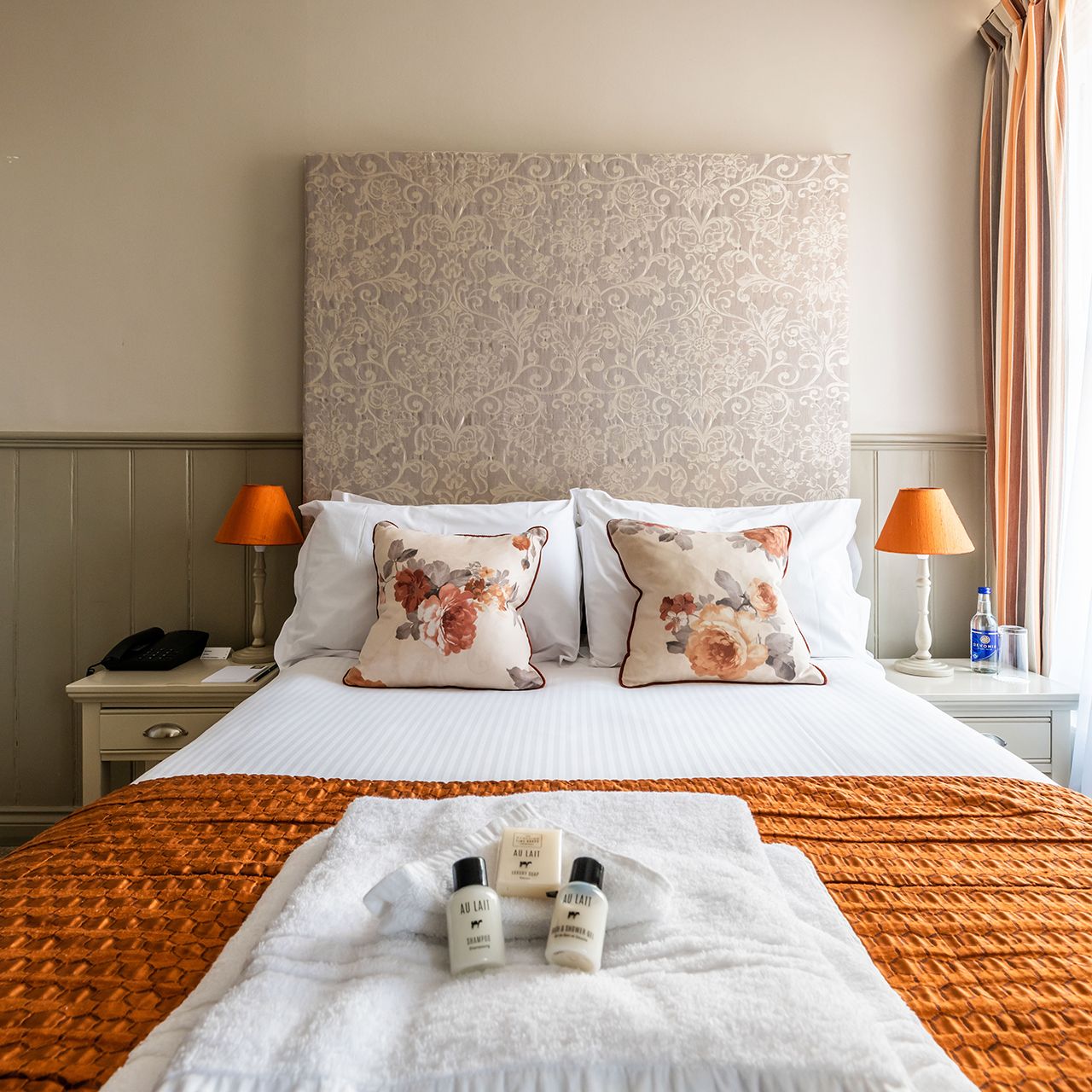 Double bed with orange throw, towels and toiletries on bed
