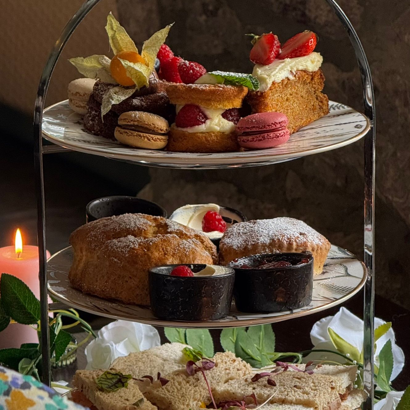 Elegant afternoon tea spread with dainty sandwiches, warm scones, and indulgent pastries served on a tiered stand, perfect for a cosy, candlelit treat.