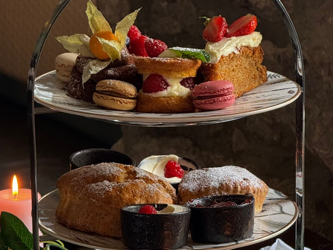 Elegant afternoon tea spread with dainty sandwiches, warm scones, and indulgent pastries served on a tiered stand, perfect for a cosy, candlelit treat.