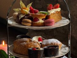 Elegant afternoon tea spread with dainty sandwiches, warm scones, and indulgent pastries served on a tiered stand, perfect for a cosy, candlelit treat.