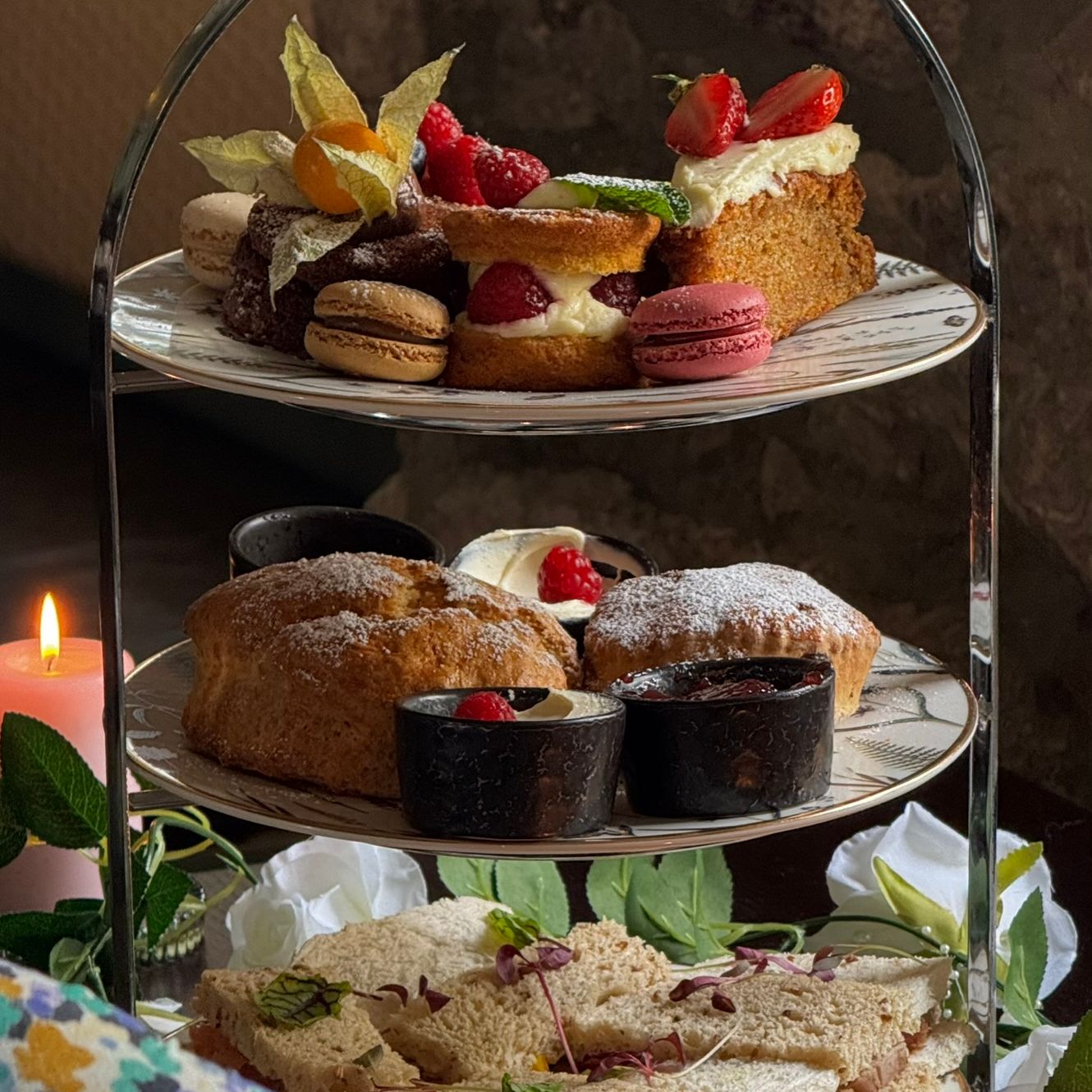 Elegant afternoon tea spread with dainty sandwiches, warm scones, and indulgent pastries served on a tiered stand, perfect for a cosy, candlelit treat.