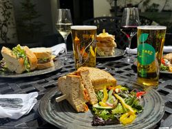 A selection of sandwiches, salads, wine, and cider served on a sunny outdoor table, perfect for a relaxed al fresco lunch in a garden setting.