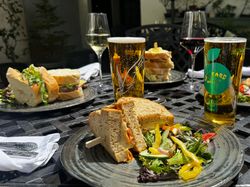A selection of sandwiches, salads, wine, and cider served on a sunny outdoor table, perfect for a relaxed al fresco lunch in a garden setting.