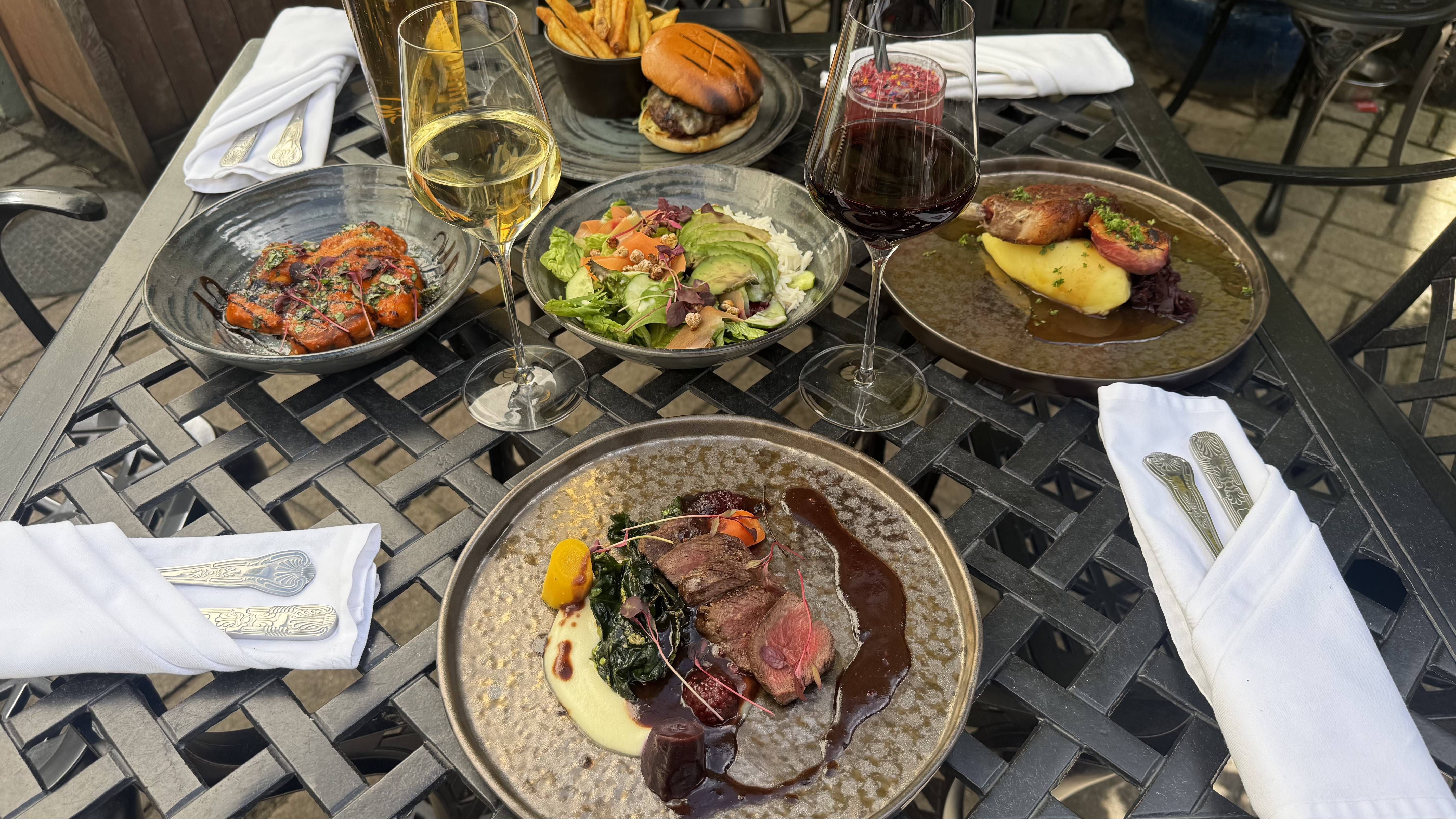 A gourmet outdoor meal with wine, showcasing elegant mains, starters, and sides on a wrought iron table, ready for al fresco dining in the sun.