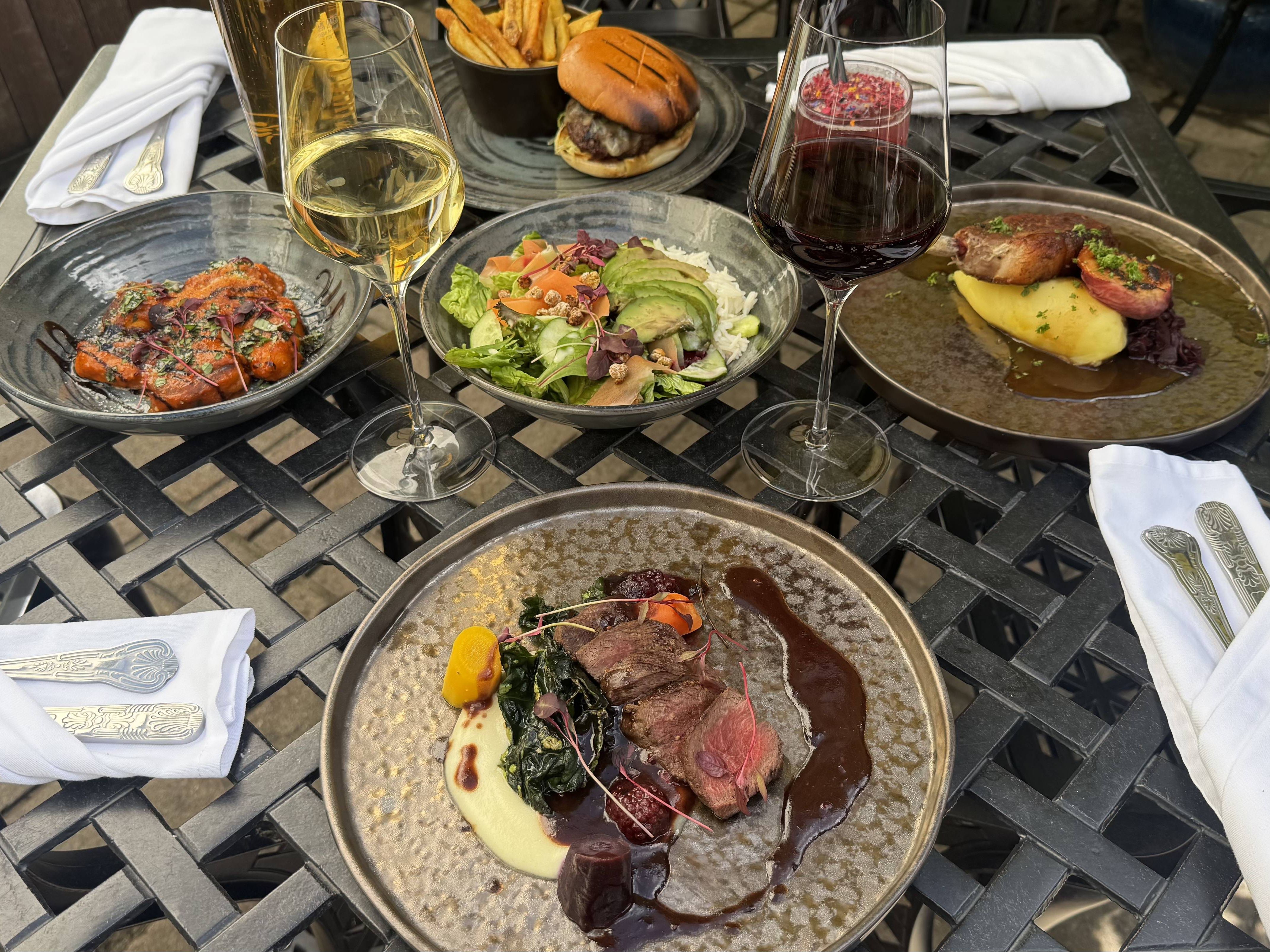 A gourmet outdoor meal with wine, showcasing elegant mains, starters, and sides on a wrought iron table, ready for al fresco dining in the sun.
