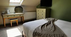 Cozy bedroom interior with green walls, a neatly made bed, a dresser, a vanity table with a round mirror, and a skylight.
