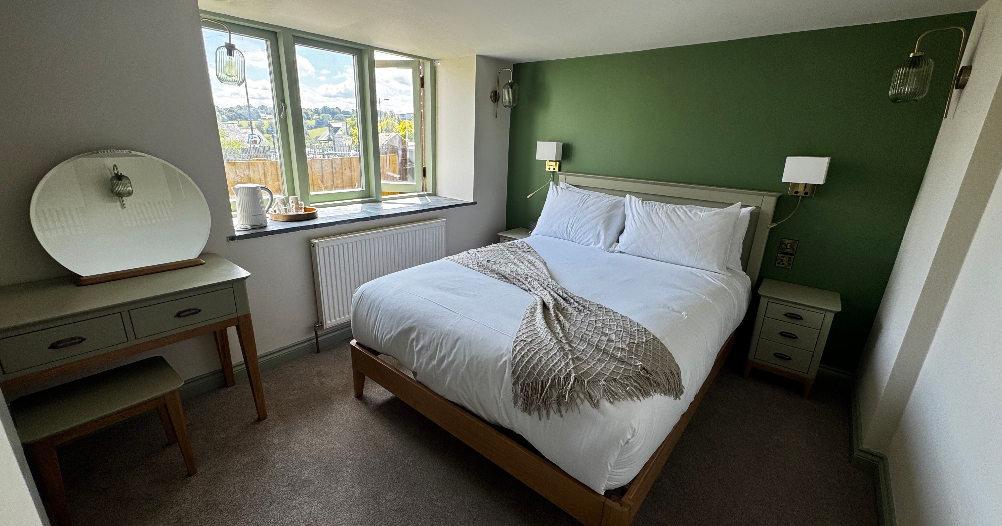 Cozy bedroom with green accent wall, white bedding, and wooden furniture.