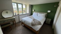 Cozy bedroom with green accent wall, white bedding, and wooden furniture.